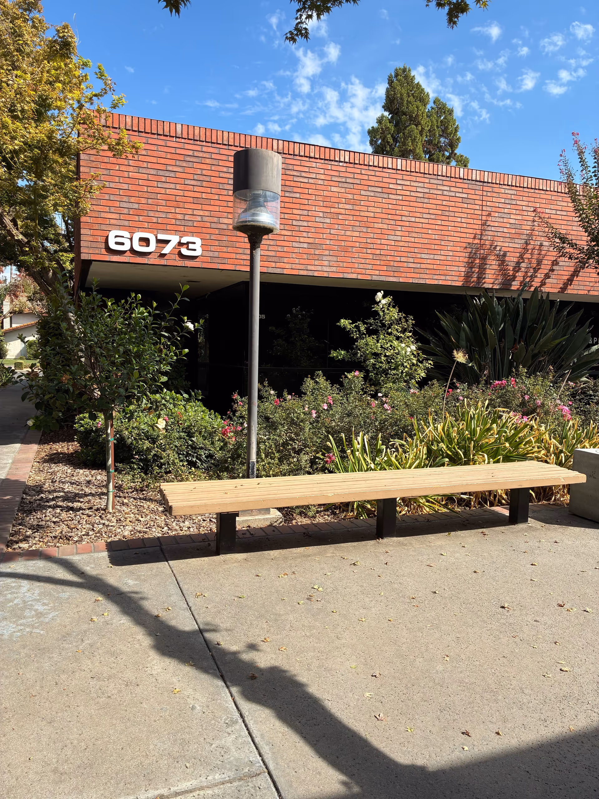 Front view of J&P Health, LLC facility with brick exterior, landscaping, and a wooden bench.