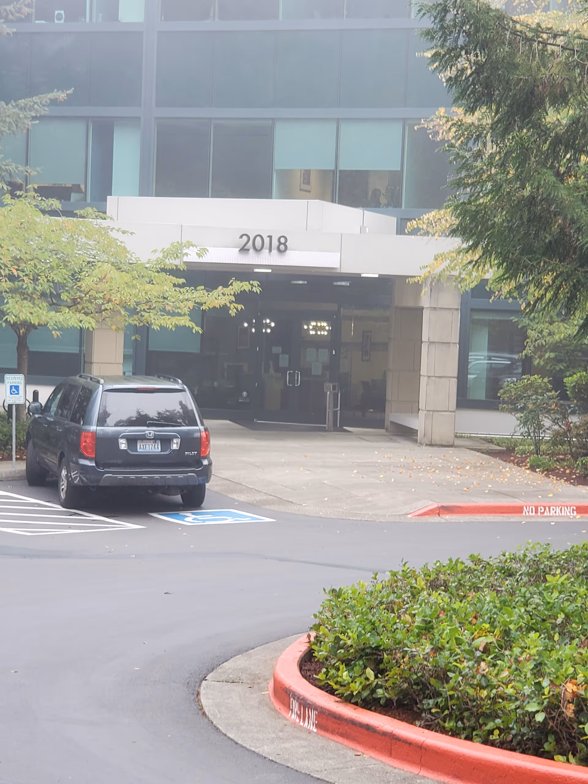 Front entrance of a modern senior living building with a parking lot in view.