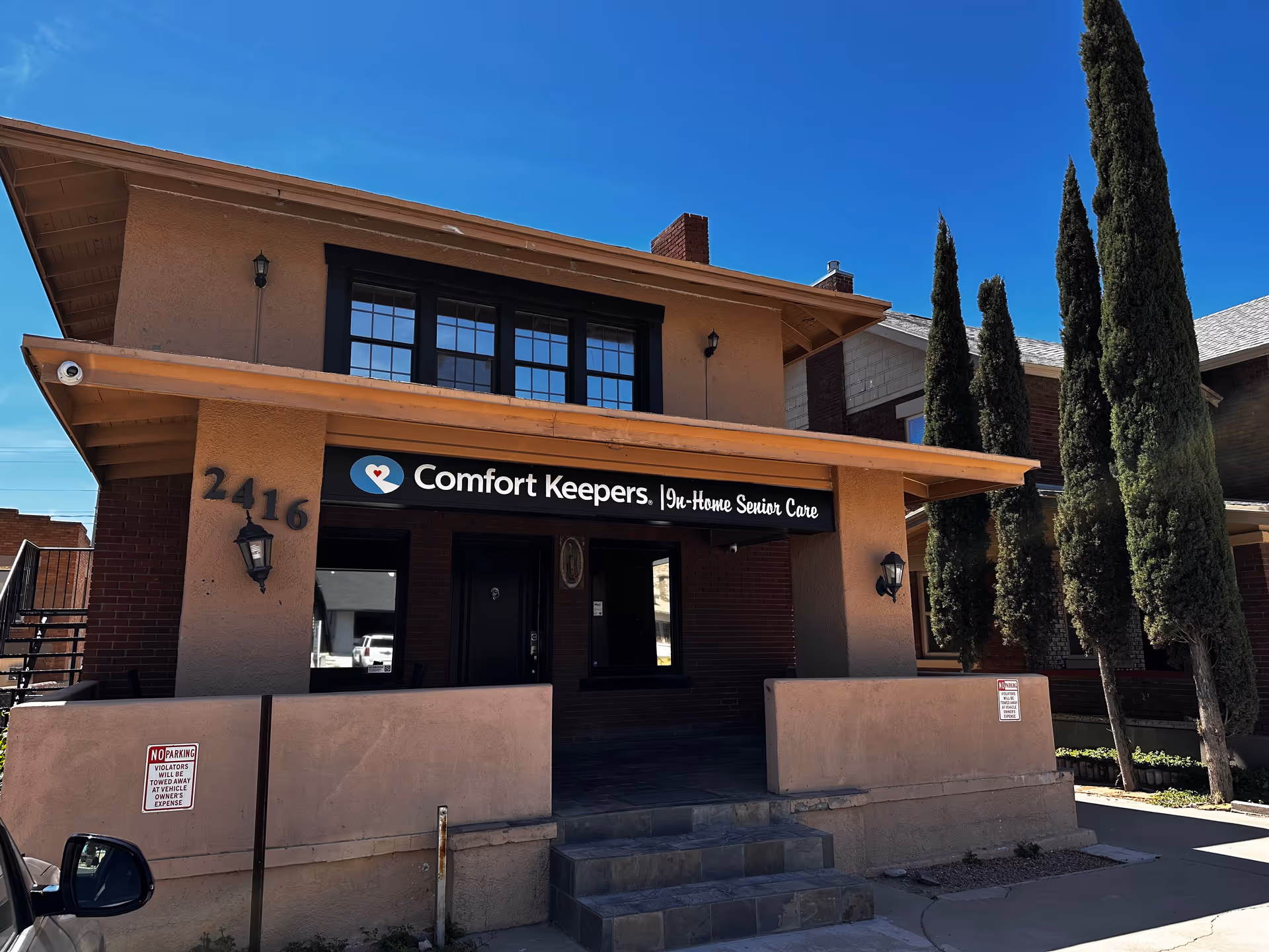 Tan building with a Comfort Keepers sign and tall trees in front