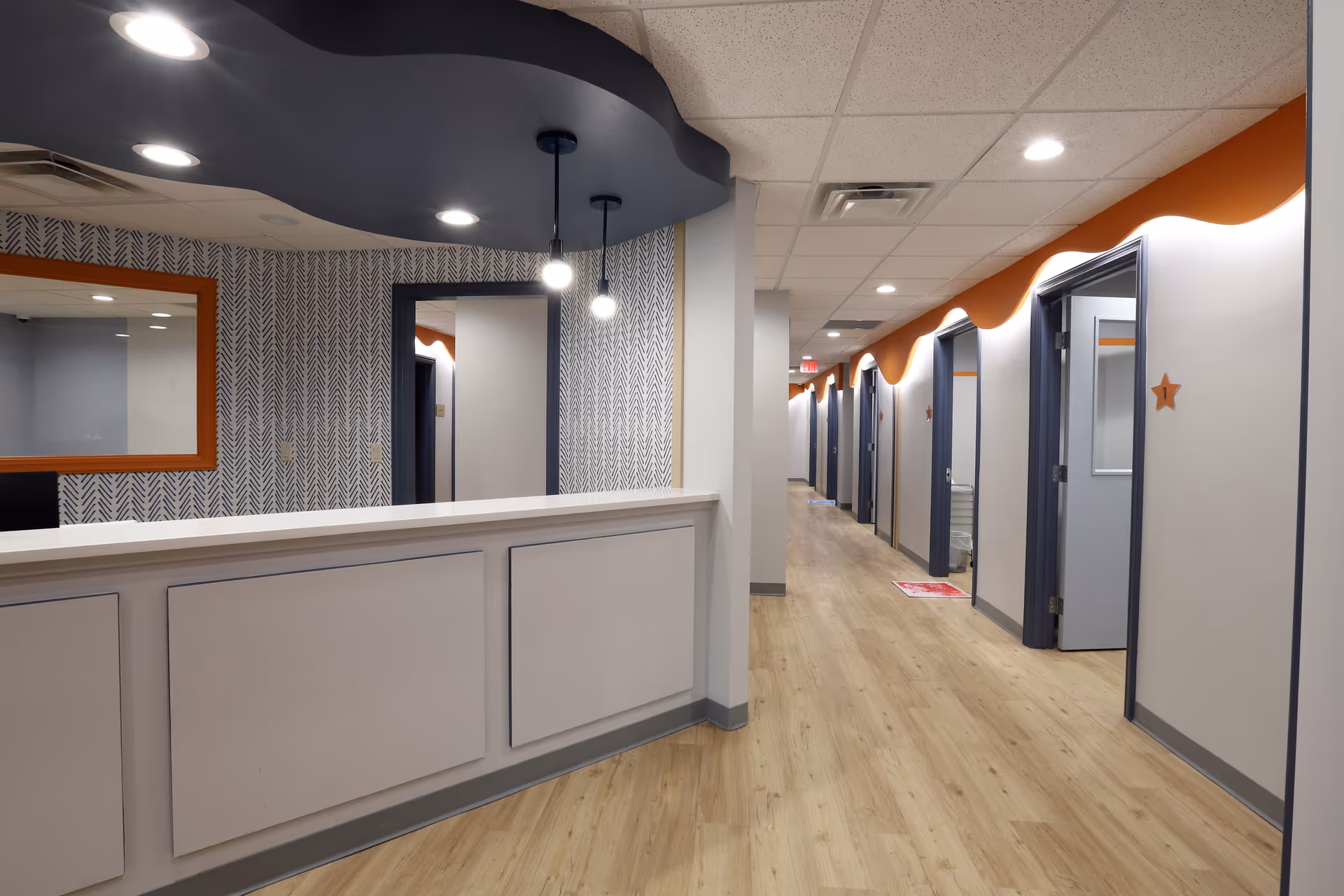Wide hallway with a reception desk, patterned wall, and multiple door rooms in a senior facility.