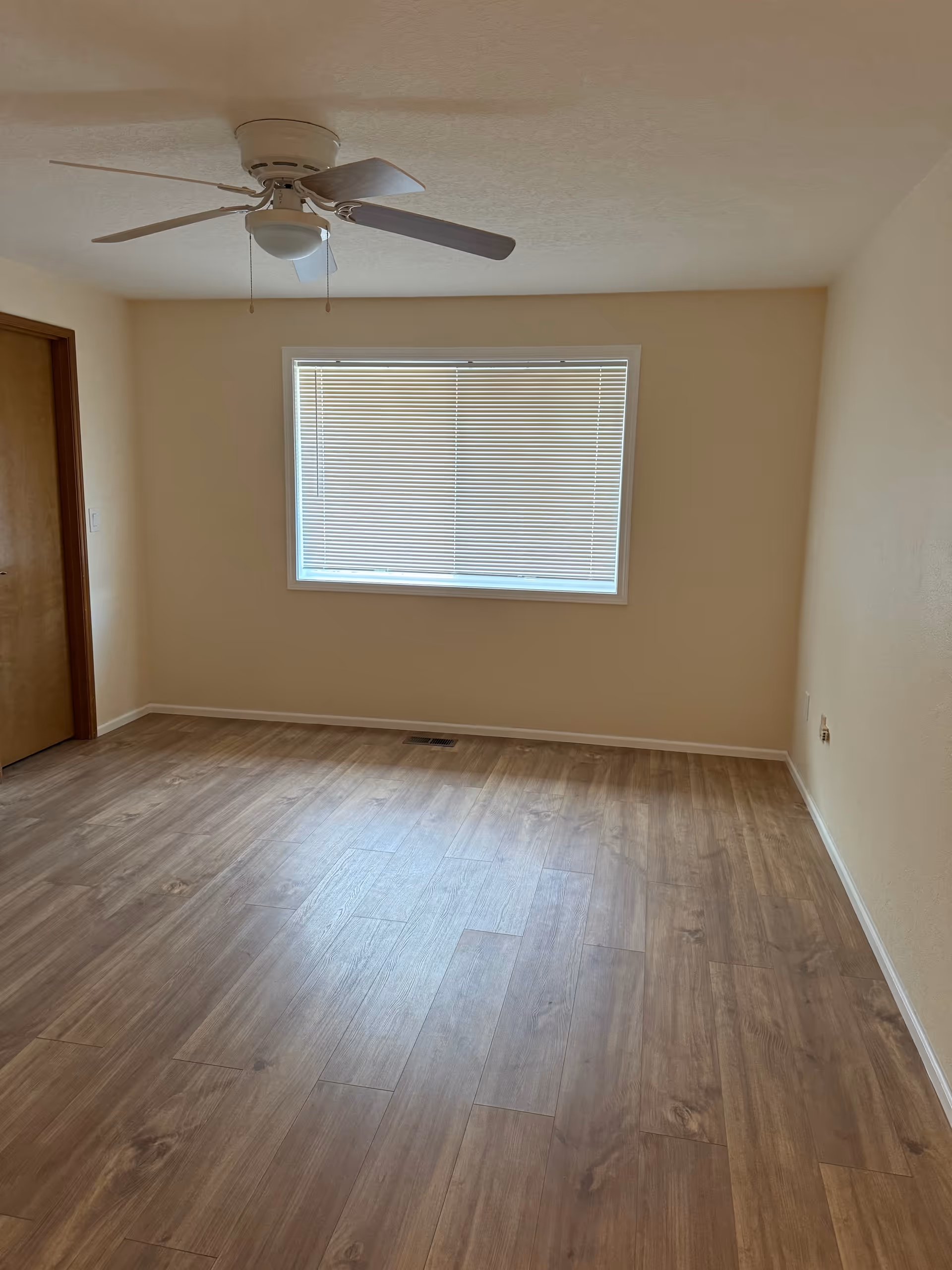 Empty beige room with window blinds, wooden floor, and ceiling fan.