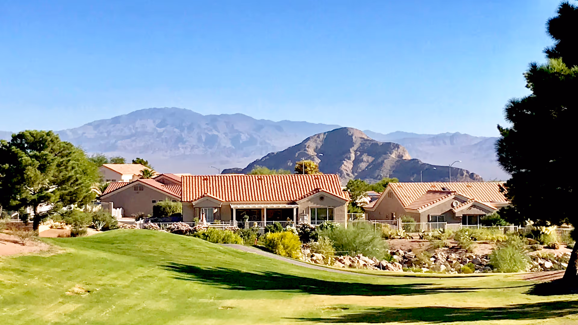 Outdoor view of Sun City Summerlin houses with red-tiled roofs and mountains.