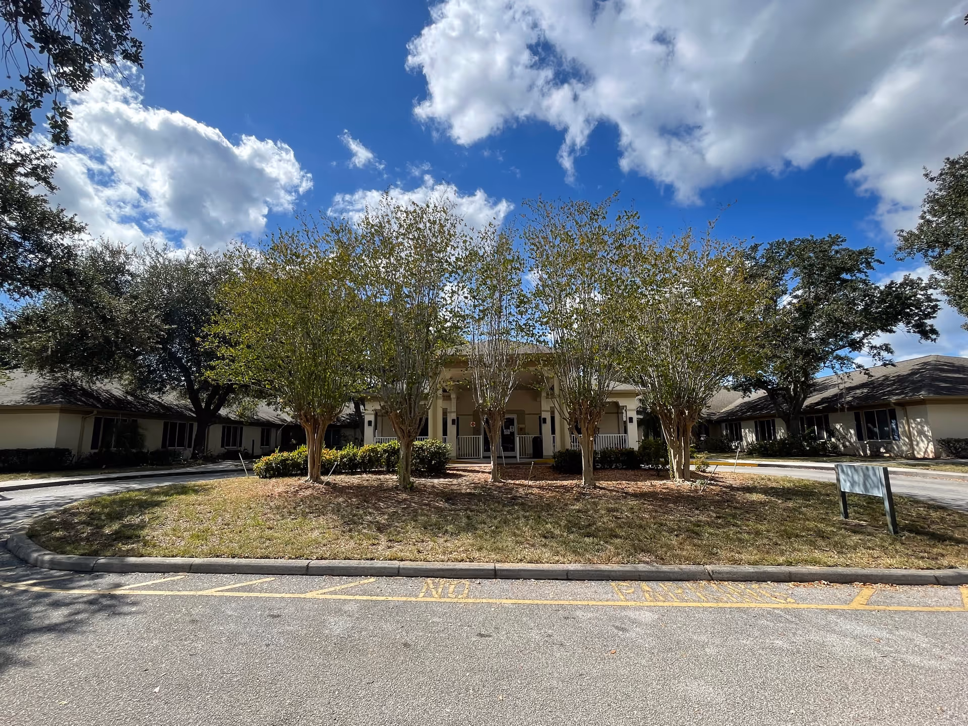 Front view of a single-story senior living facility with a circular driveway and trees.