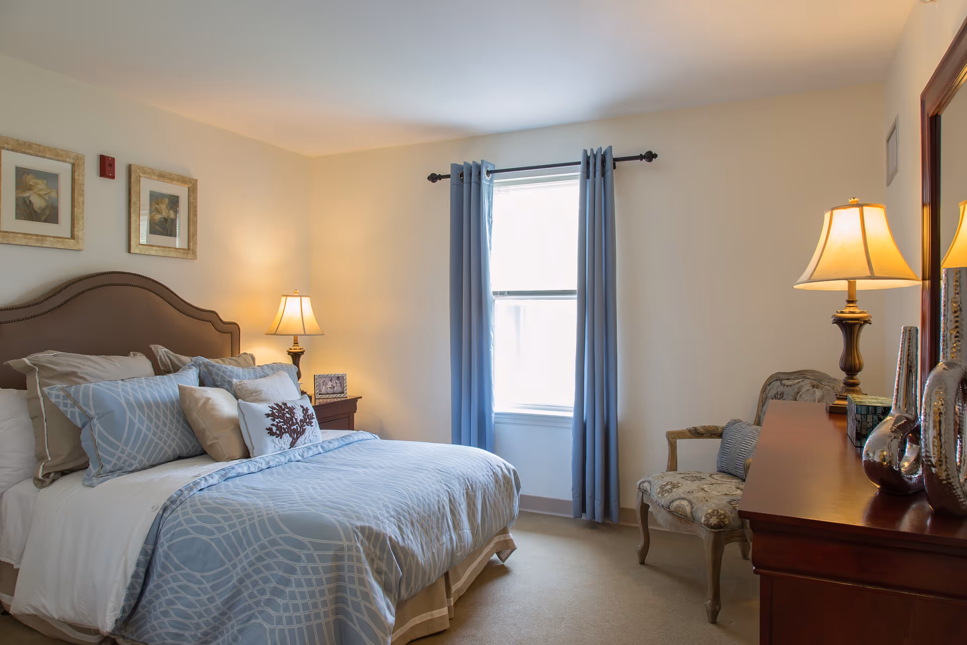 Cozy bedroom featuring a large bed, nightstands, lamps, and blue curtains.