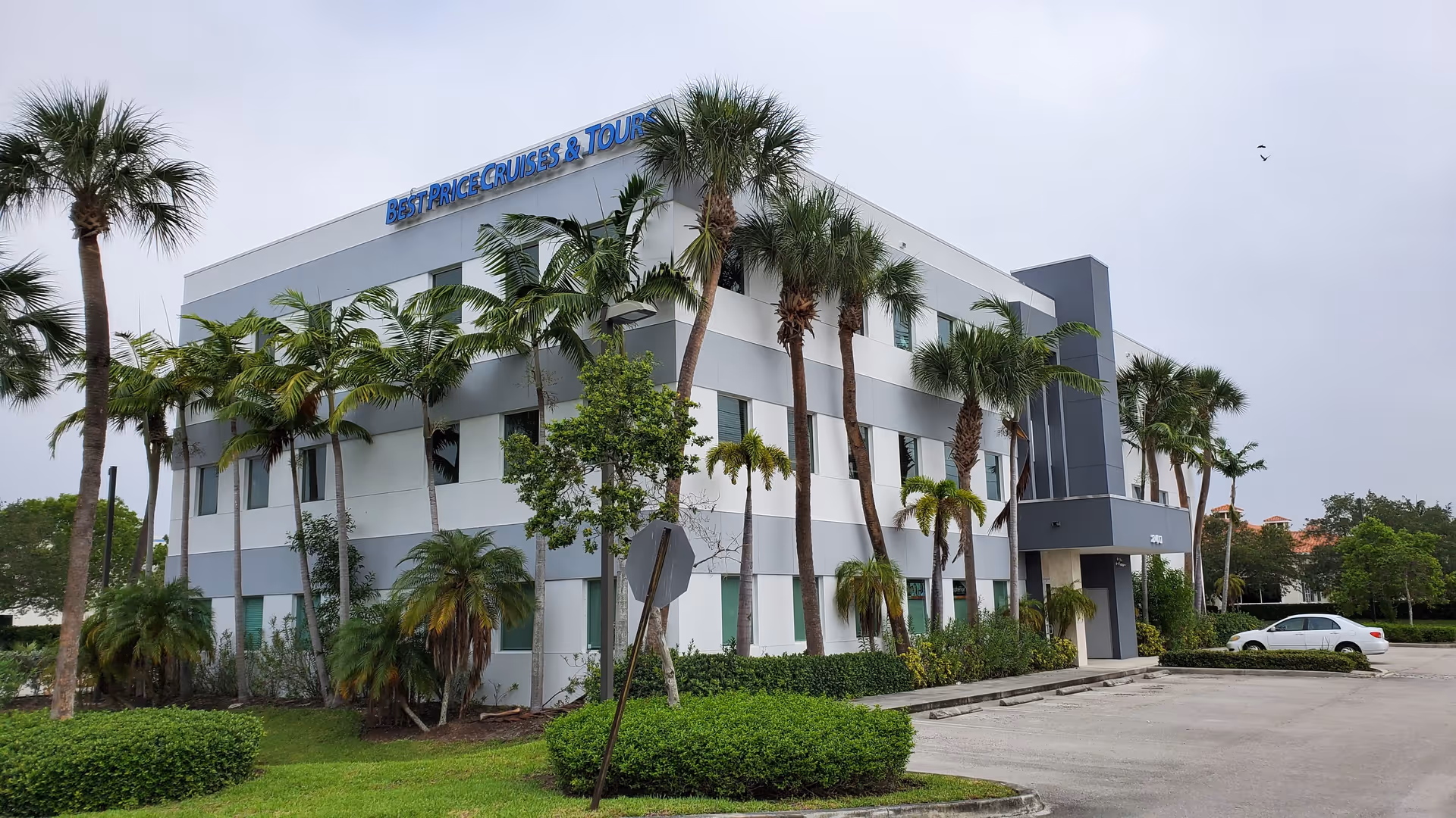 Modern three-story building with palm trees and a cloudy sky.