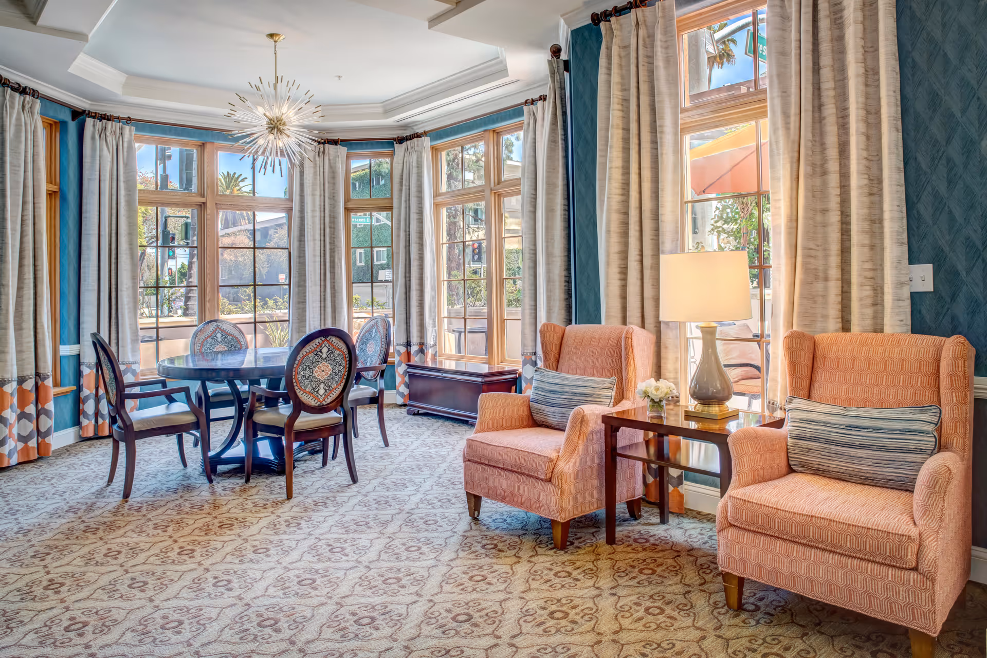 Bright Sunrise of Beverly Hills living room with peach armchairs, a round table, and large windows.