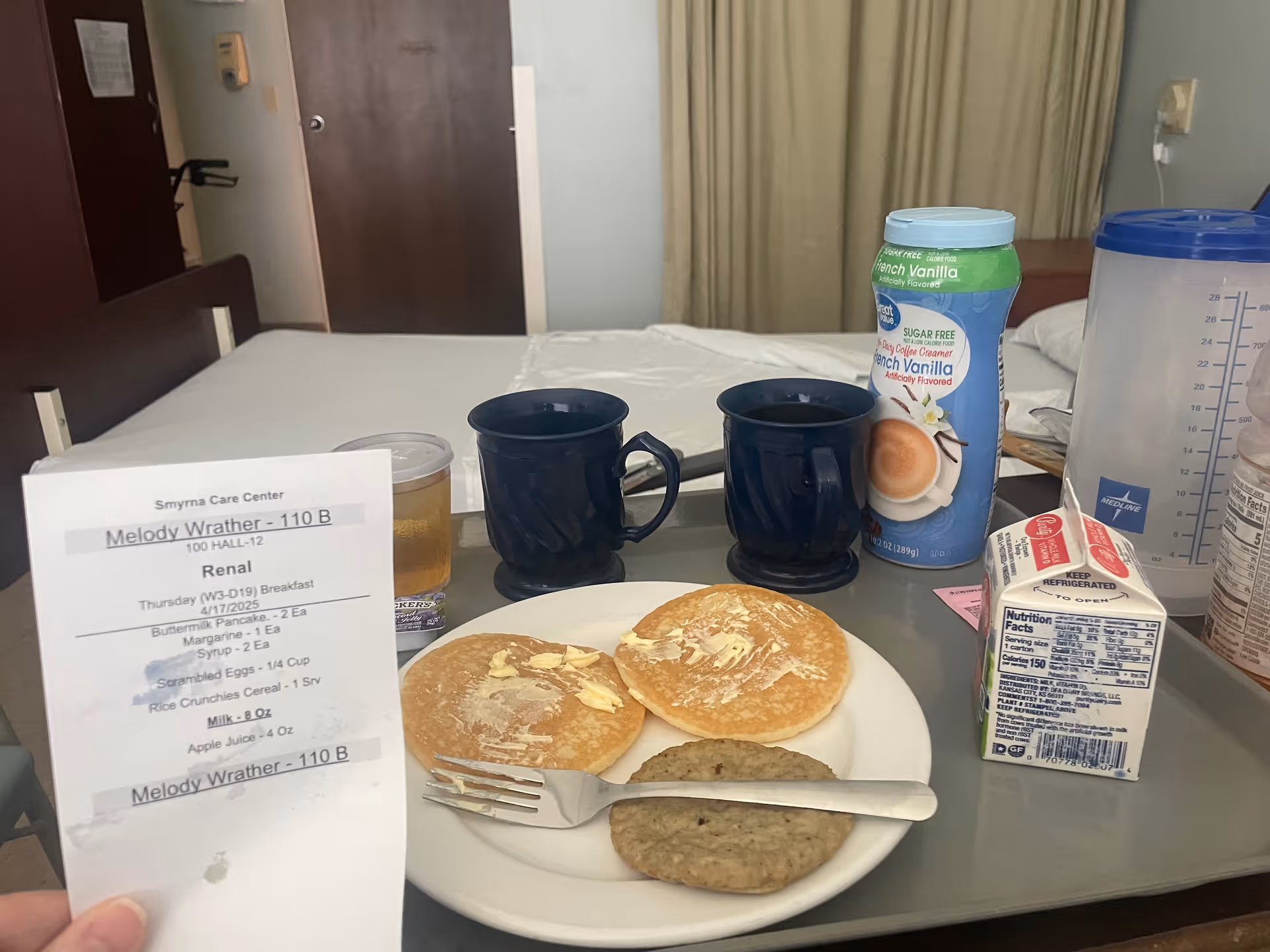 In-room meal tray on a bed with pancakes, sausage, milk, juice in a senior living room.