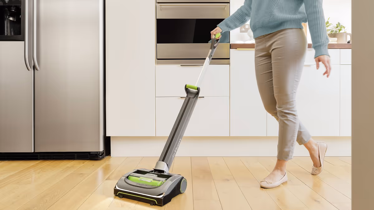 Person pushes a floor cleaning device across a bright kitchen floor with stainless appliances