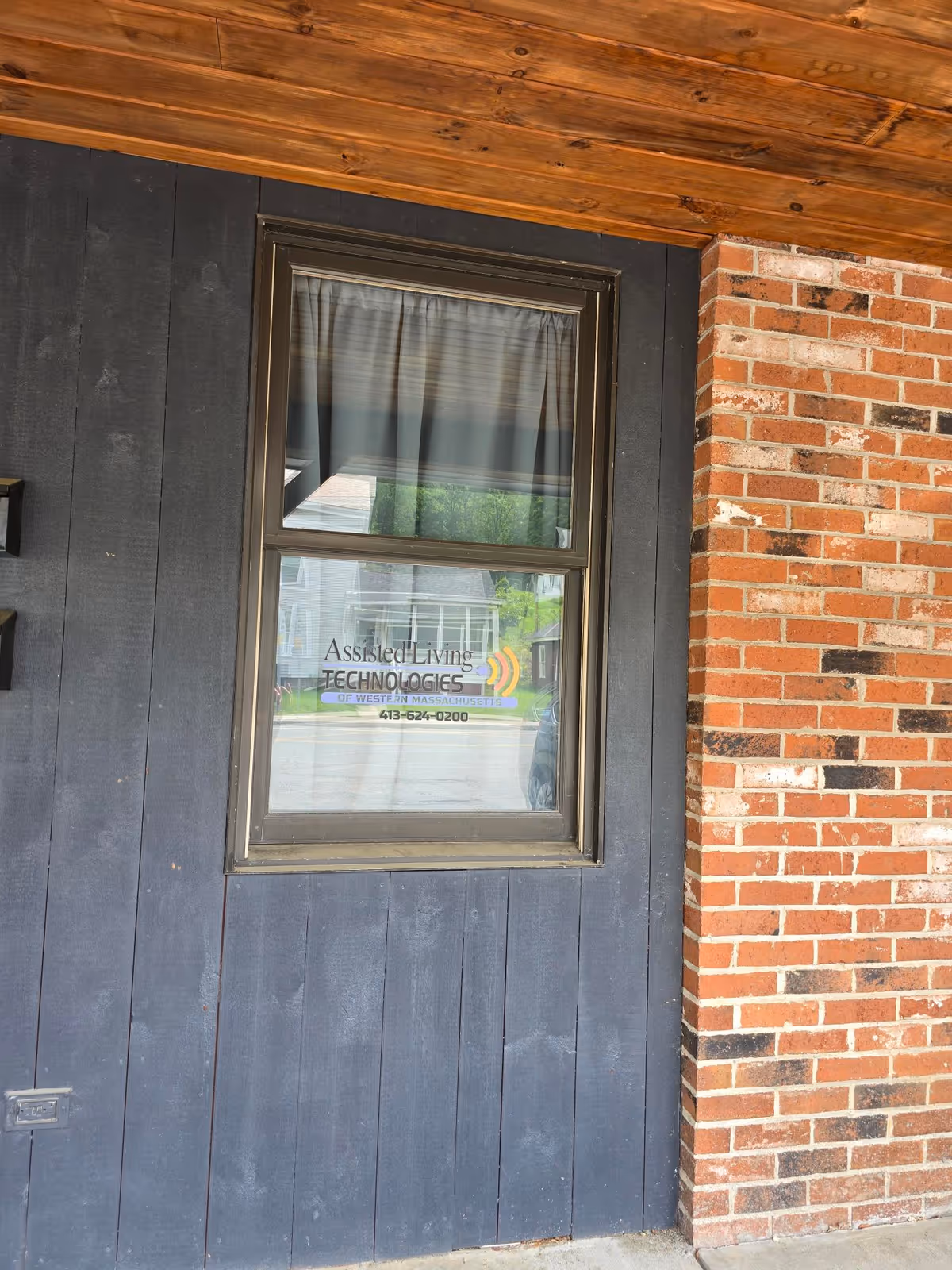 Exterior view of a brick and dark wood wall with a window displaying a facility sign.