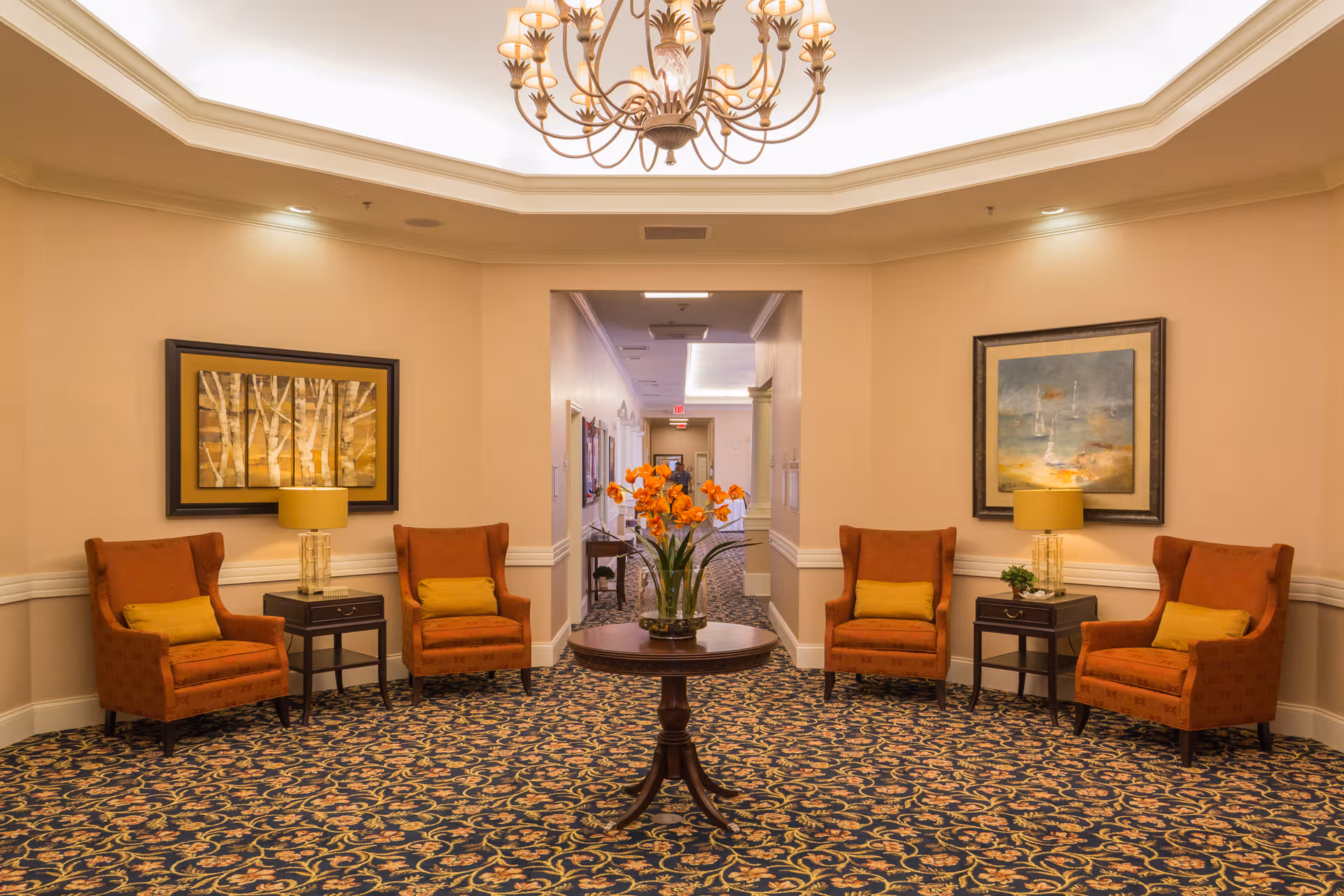 Elegant hotel-style lobby with orange chairs, central flowers, and a chandelier.
