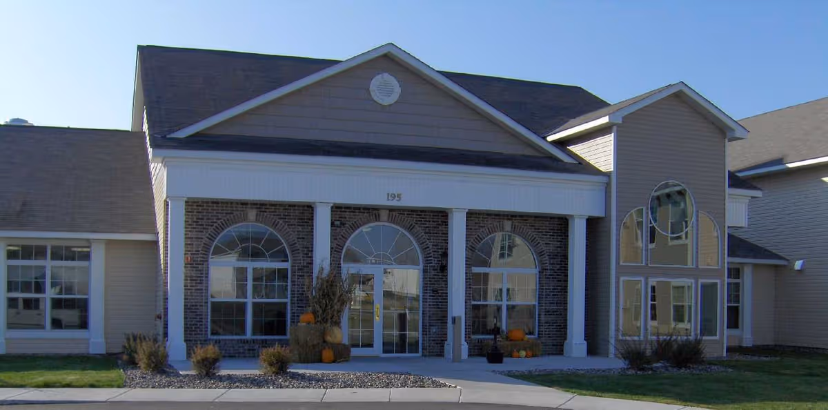Front exterior of Traditions of Owatonna senior living with pumpkins at entrance.