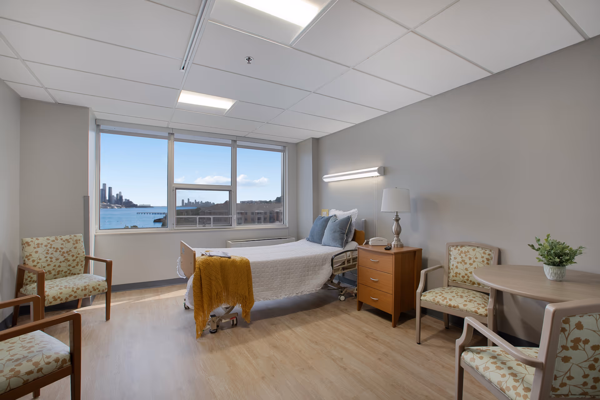 Bright patient bedroom in a senior living facility with a large window view.
