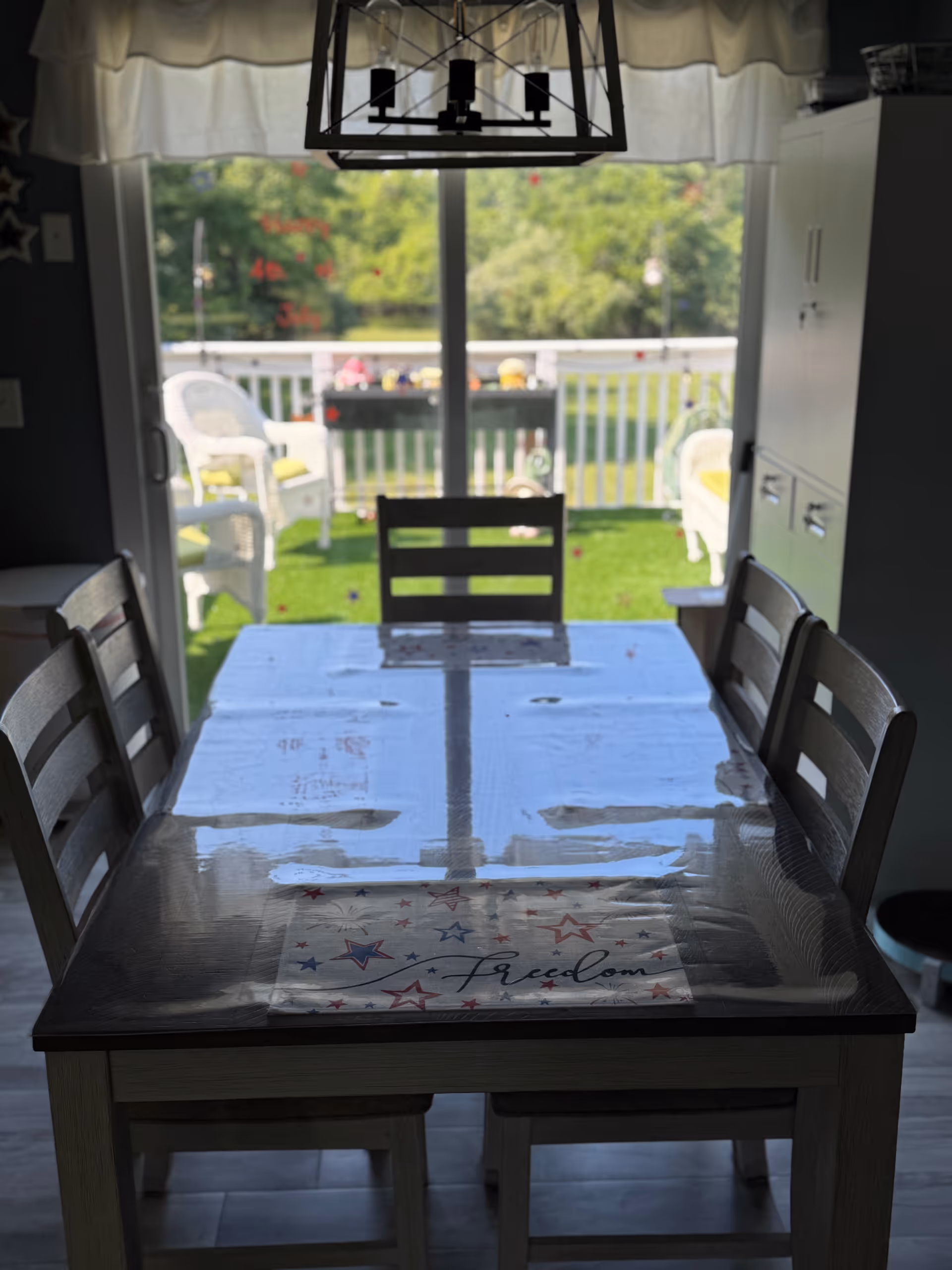 Dining table with plastic cover and patriotic placemat, facing a bright outdoor deck.