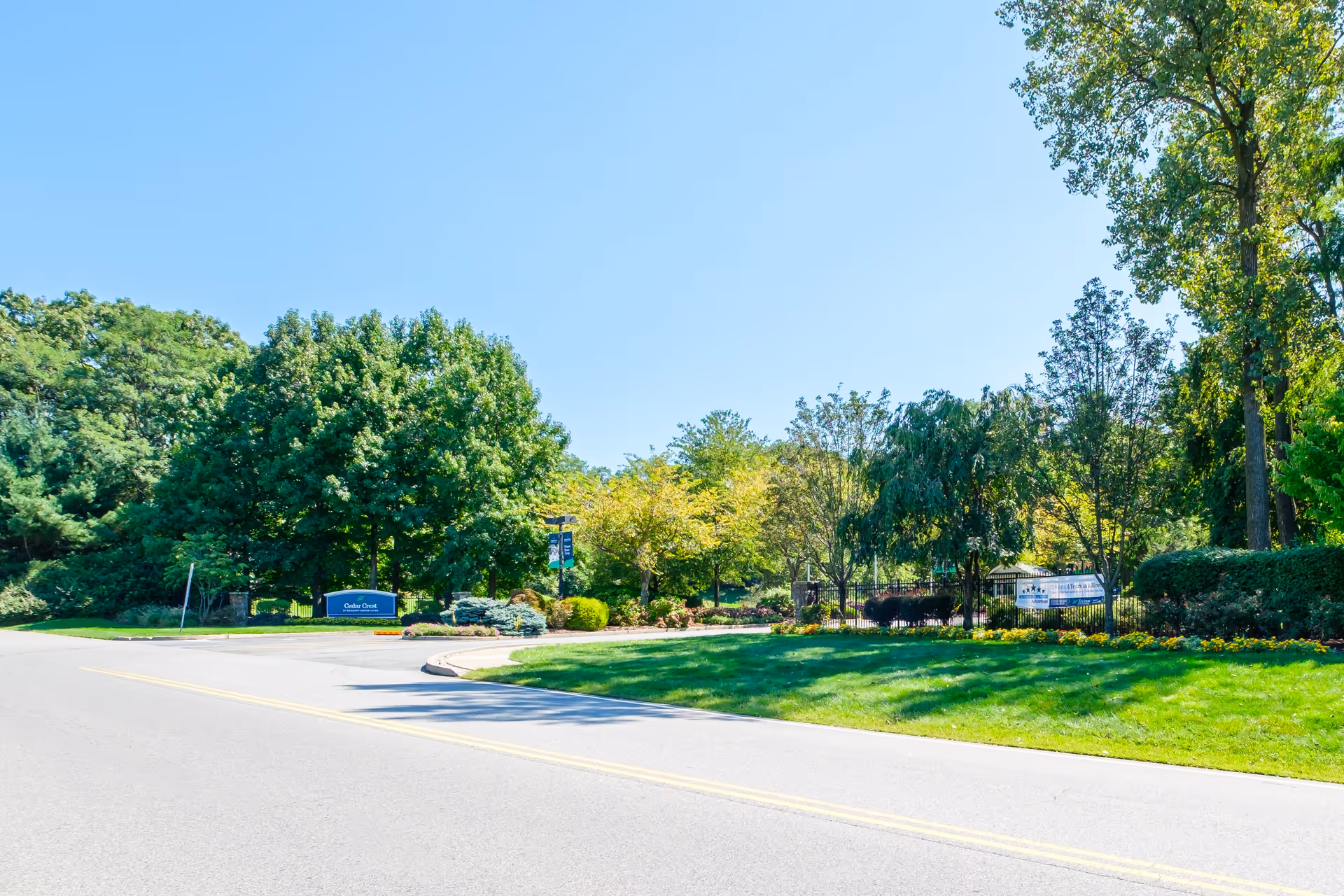 Landscaped driveway and entrance to the Cedar Crest community with lawns, trees, and a sign.