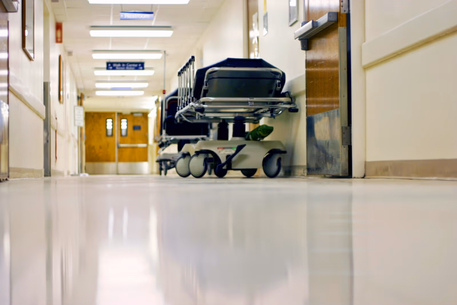 A hospital hallway with a wheeled medical stretcher parked near a door.
