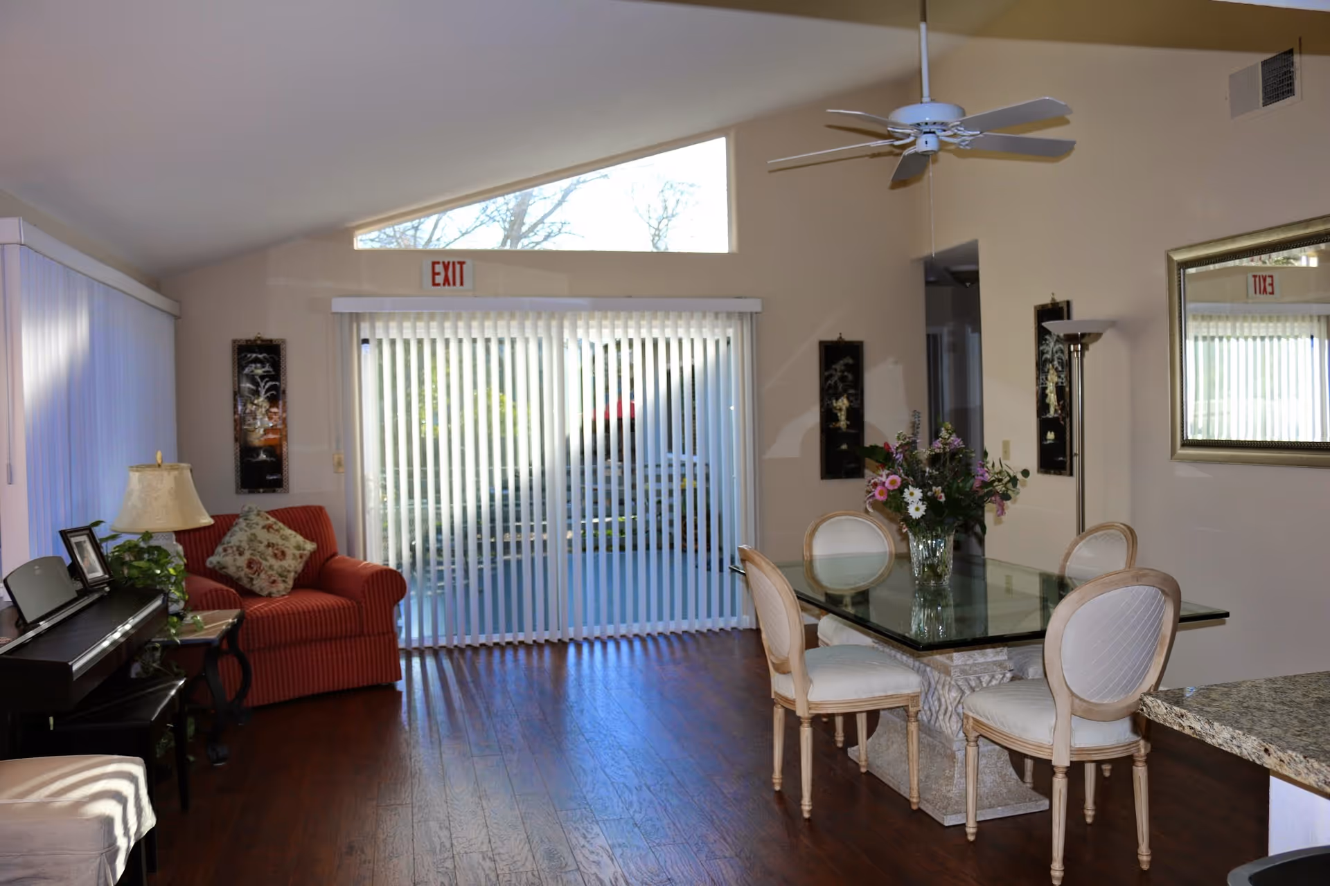 Open living and dining area with glass top table, chairs, red sofa, and sliding glass door.