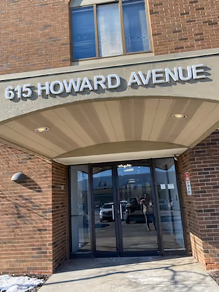 Brick building entrance with glass doors and an arched canopy labeled 615 Howard Avenue.