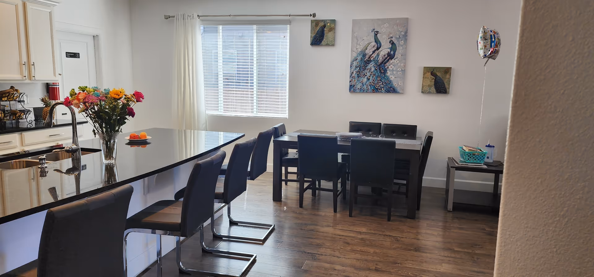 Open kitchen and dining area with a long island, bar stools, flowers, and peacock wall art.