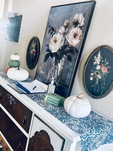 Decorative hallway console features framed florals, pumpkins, and a blue patterned runner.