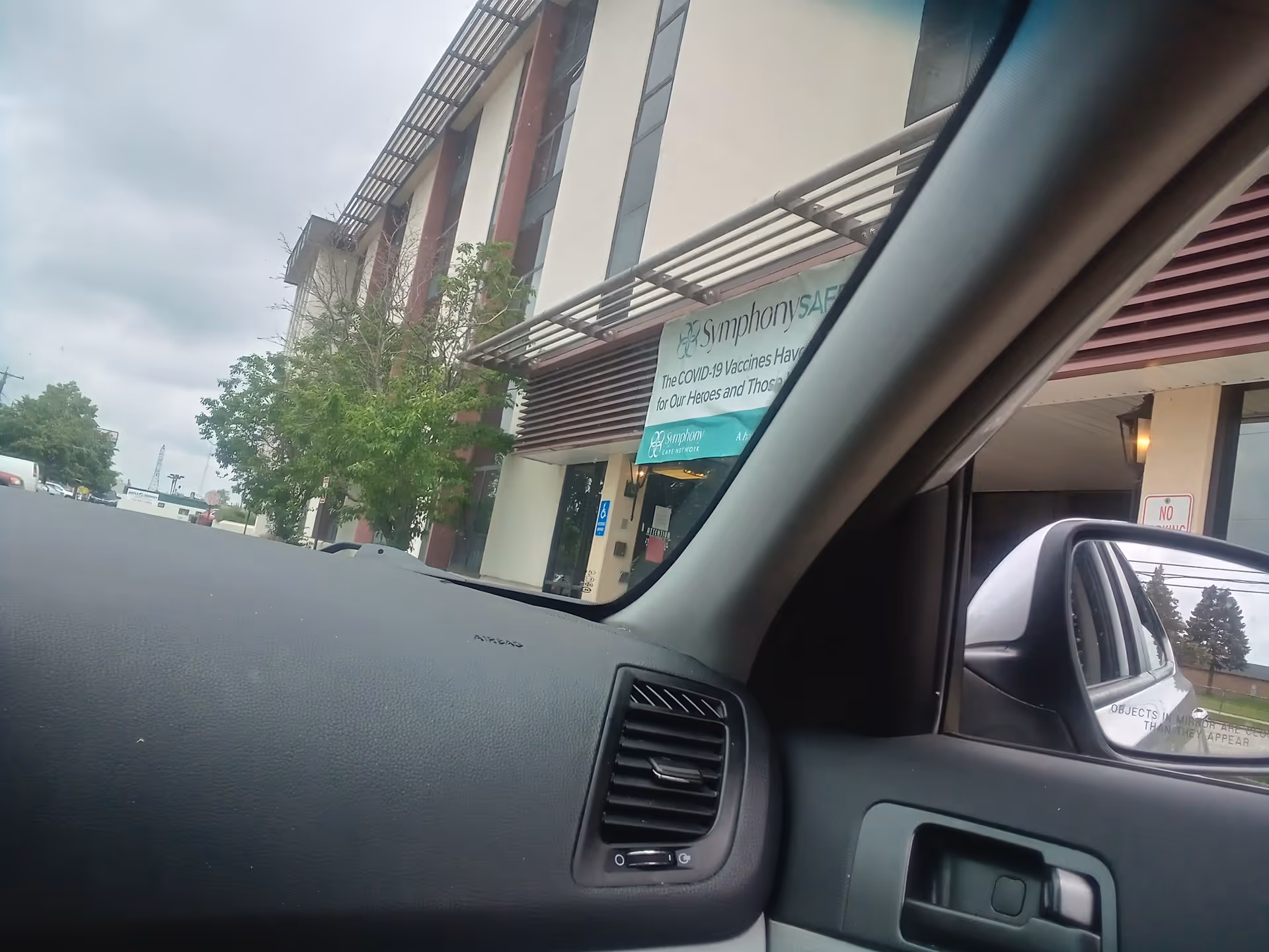 Dashboard view from a car shows a building exterior with a sign near the entrance.