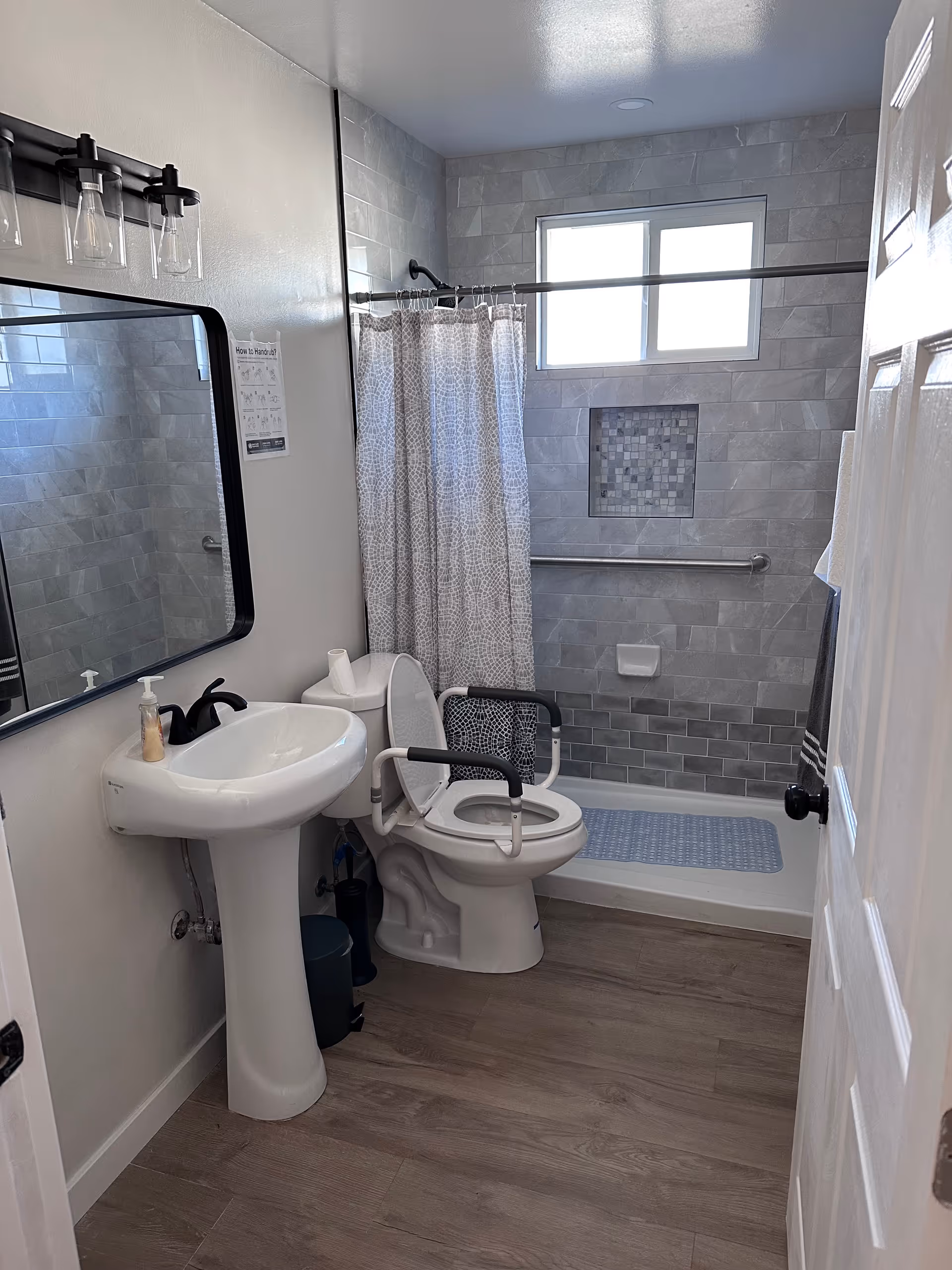 Small bathroom with sink, toilet with grab bars, and tiled shower area.