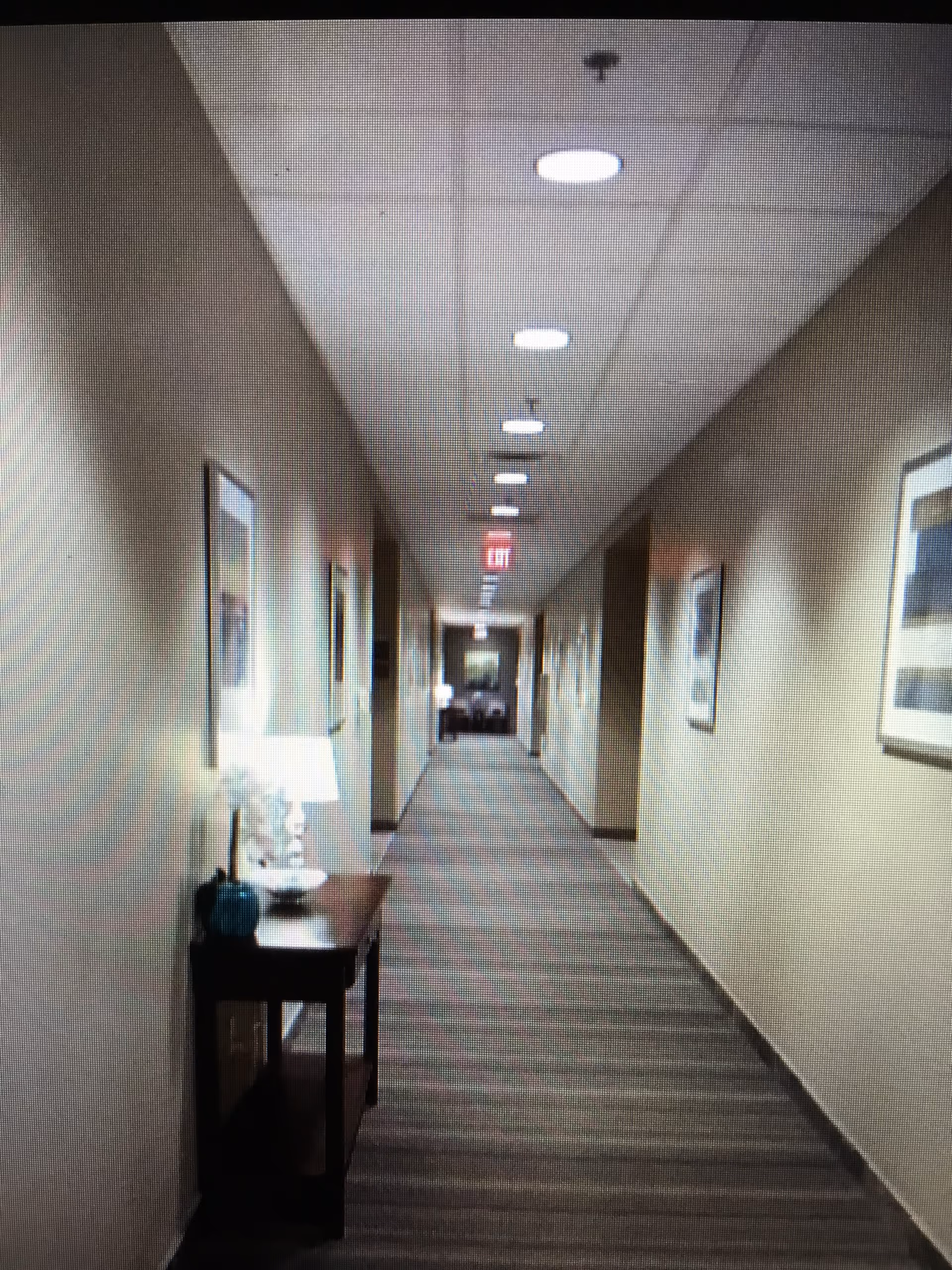 Long hallway in a senior living facility with framed art, a table, and a lamp.