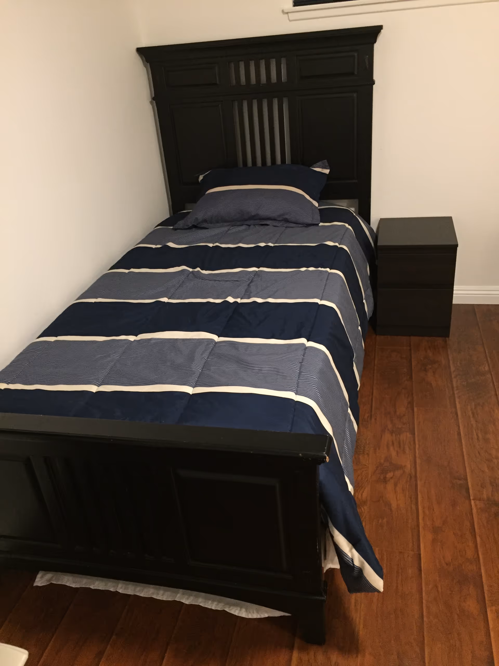 A single dark wood bed with striped blue bedding and a nightstand in a small bedroom.