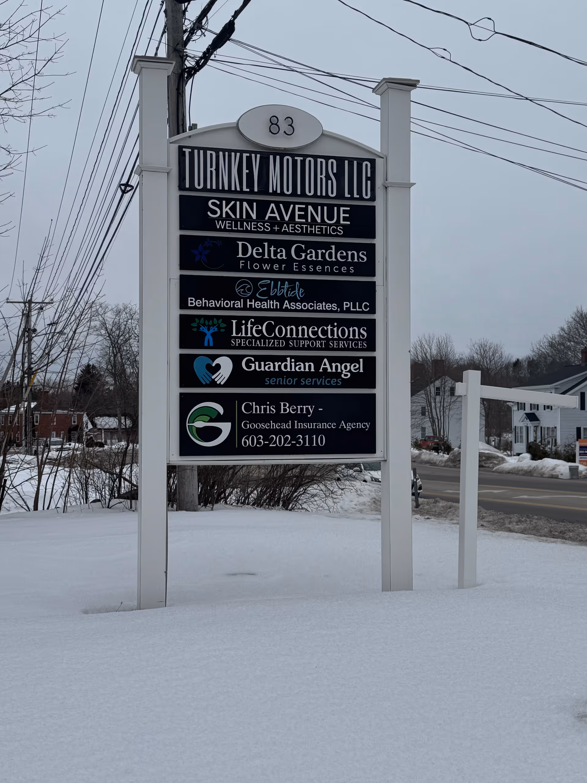 Outdoor signboard with multiple business names, including Guardian Angel Senior Services, on a snowy lot.