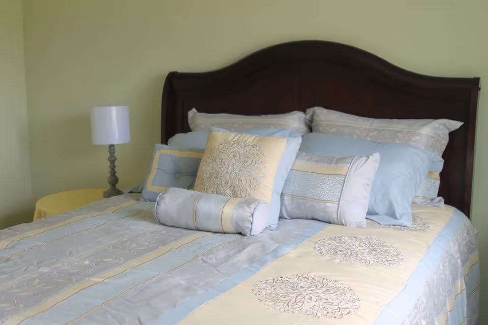 A neatly made bed with blue and beige bedding and a dark wood headboard.