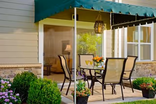 Outdoor patio with table and chairs under a green awning beside a building