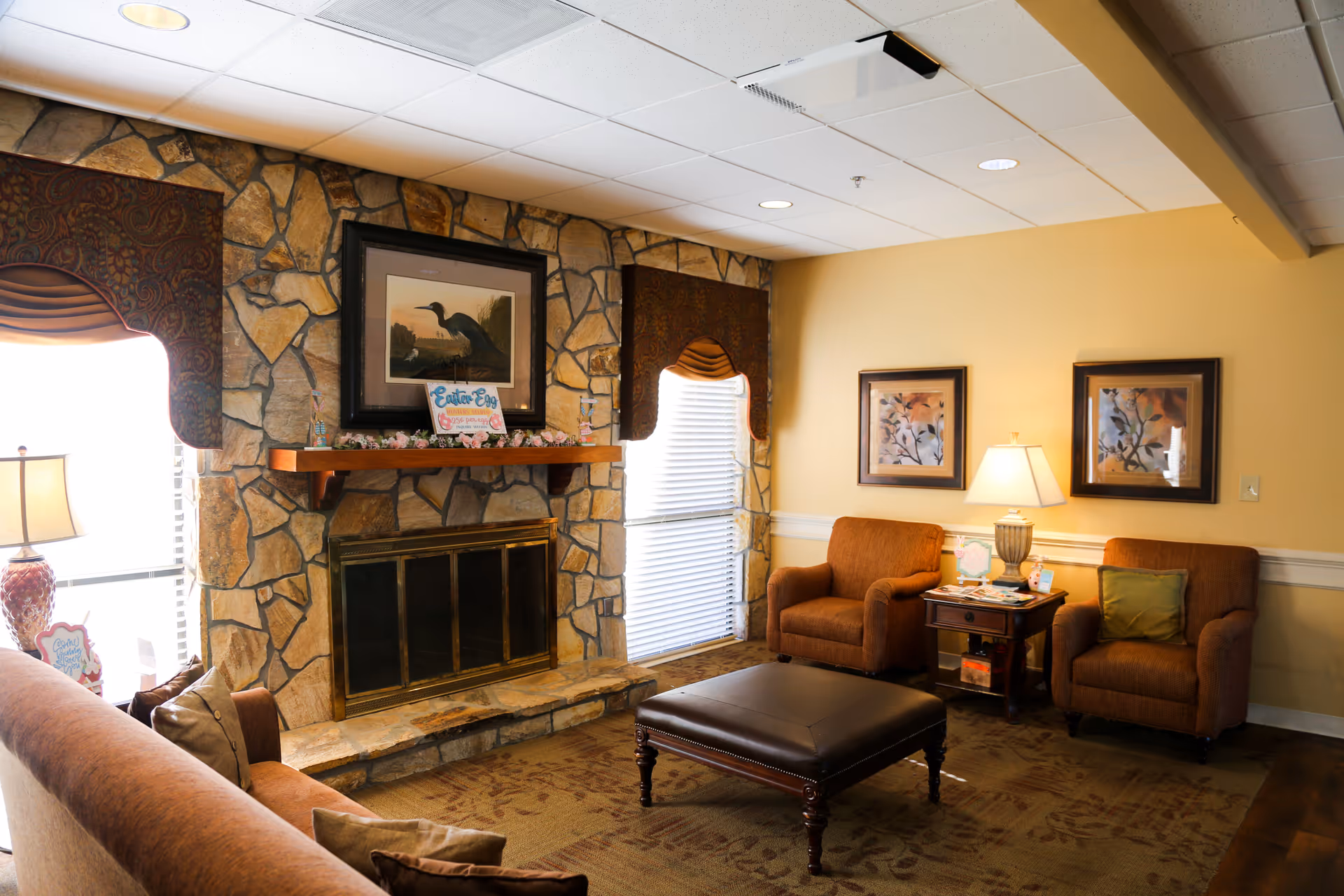 Cozy lounge with stone fireplace, seating, and artwork in a senior living facility.