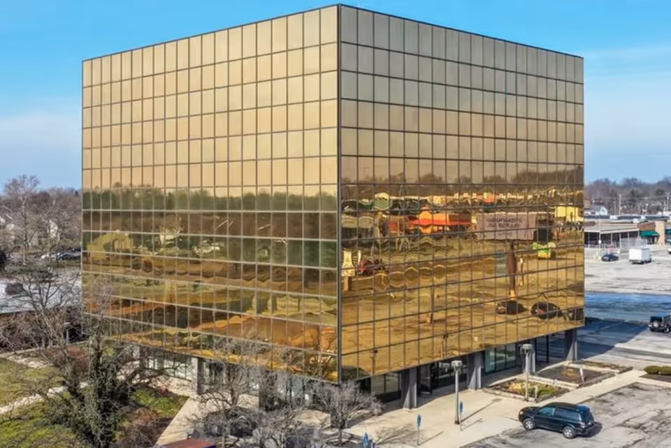 Gold-glass office building with a reflective facade beside a parking lot.