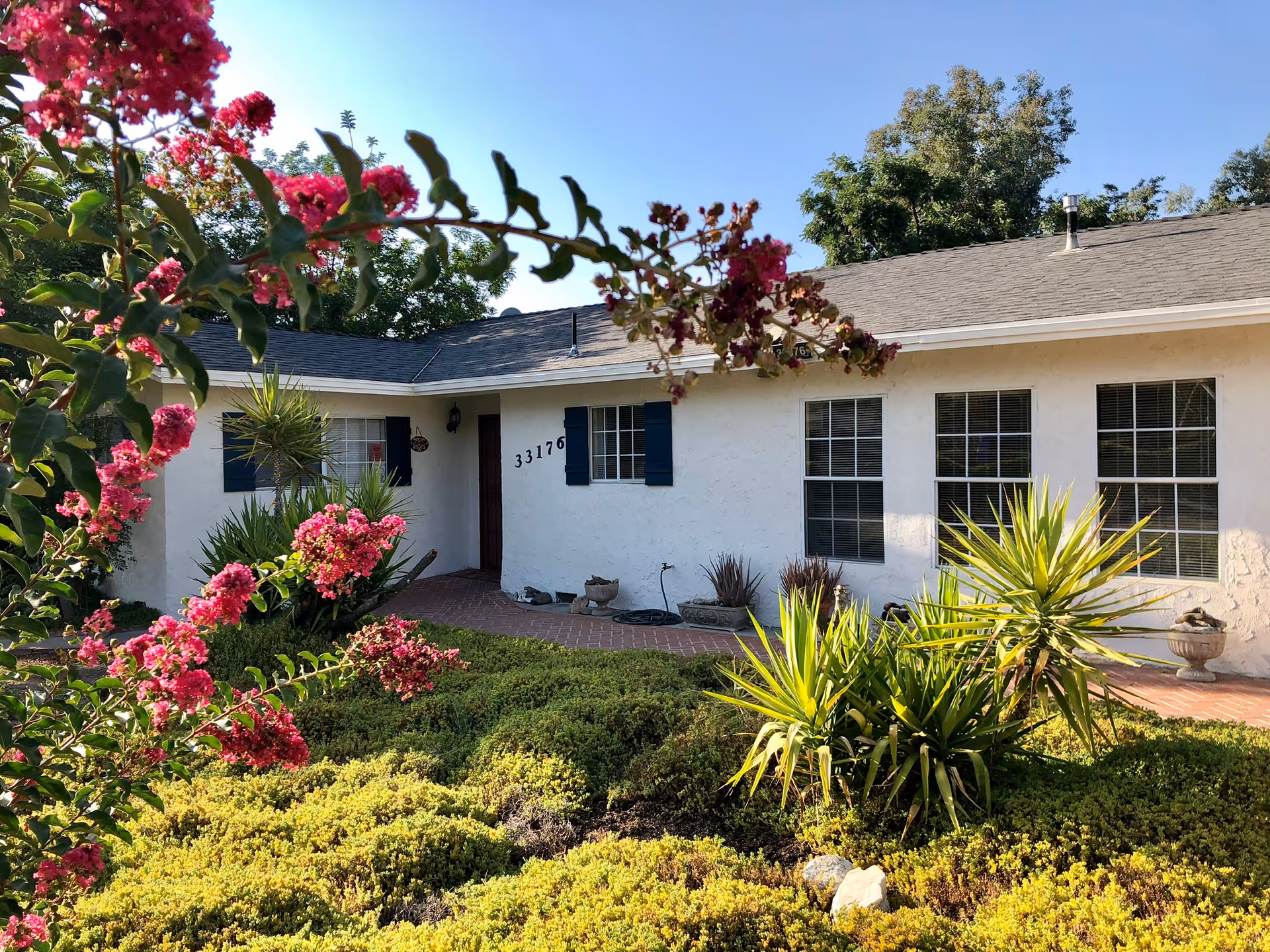 Front view of a white, single-story senior living facility with blue shutters and landscaped garden.