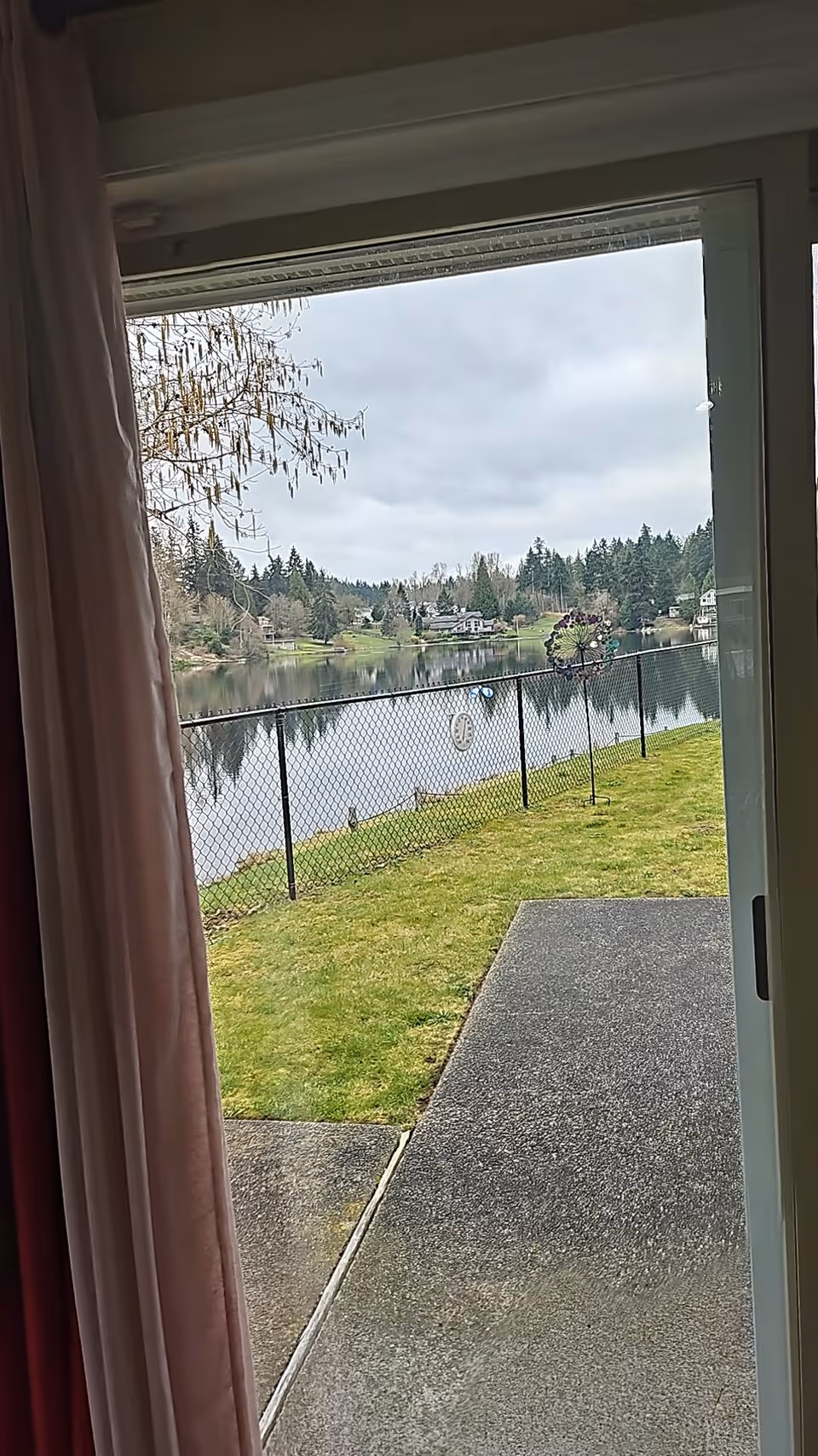 View from doorway of a grassy yard, lake beyond a chain-link fence and distant houses.