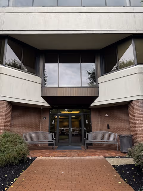 Front entrance of a brick building with glass doors and two benches outside.