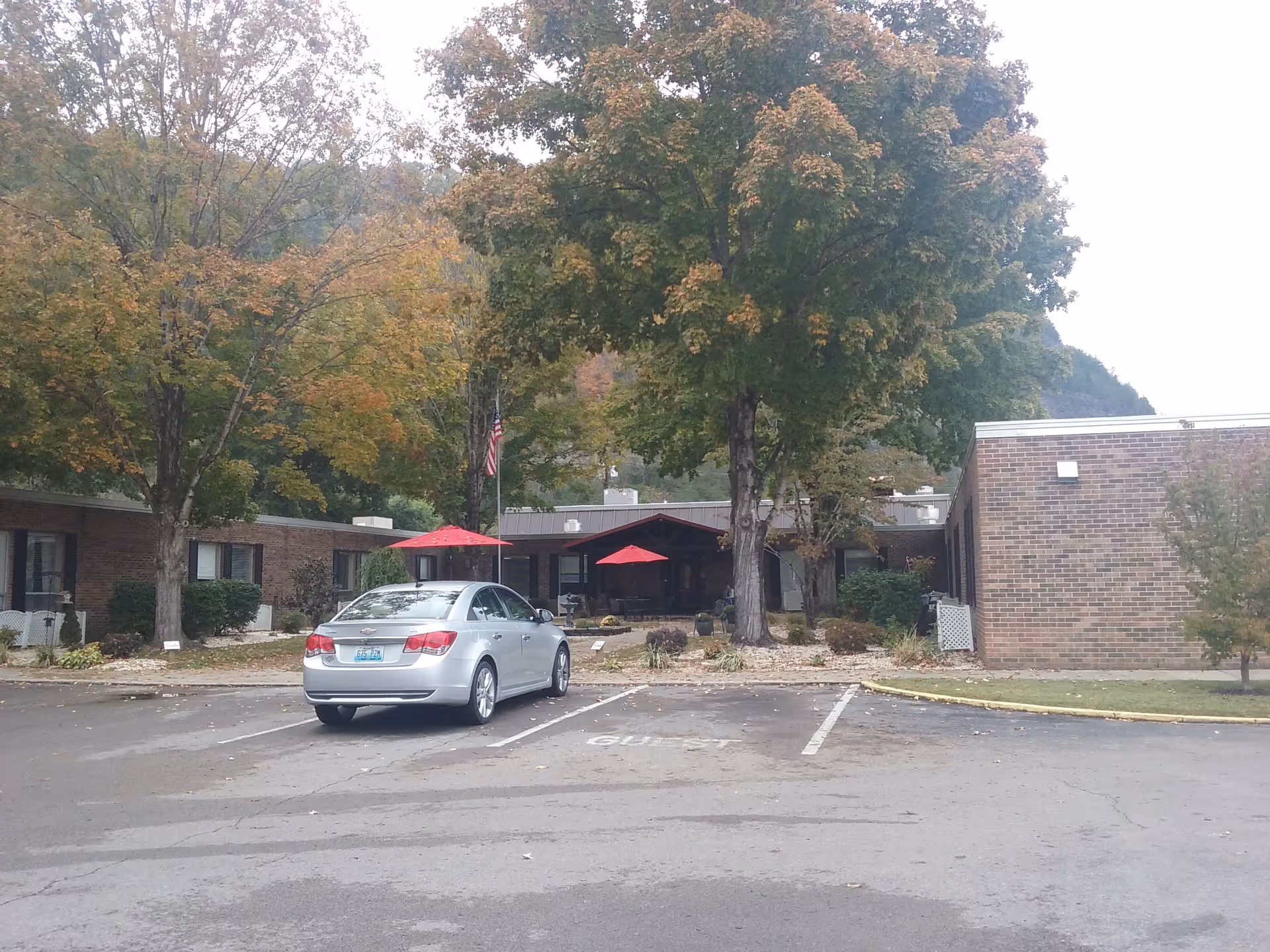 Exterior view of a nursing home entrance with trees and a parked car
