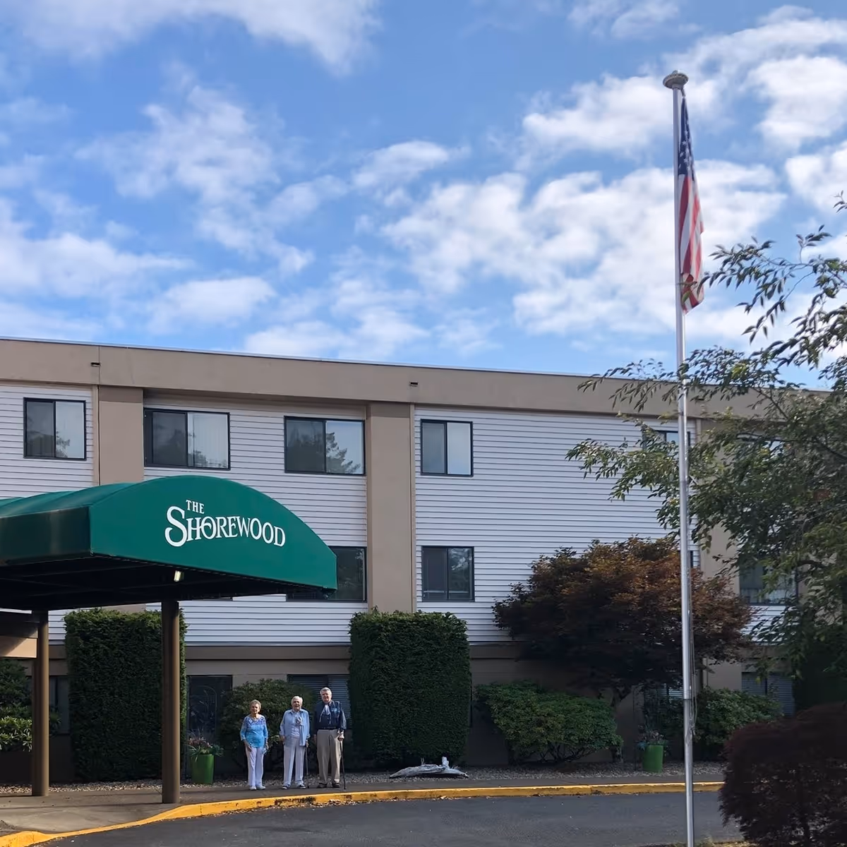 Exterior view of Shorewood Senior Living with a green awning and a small group outside.