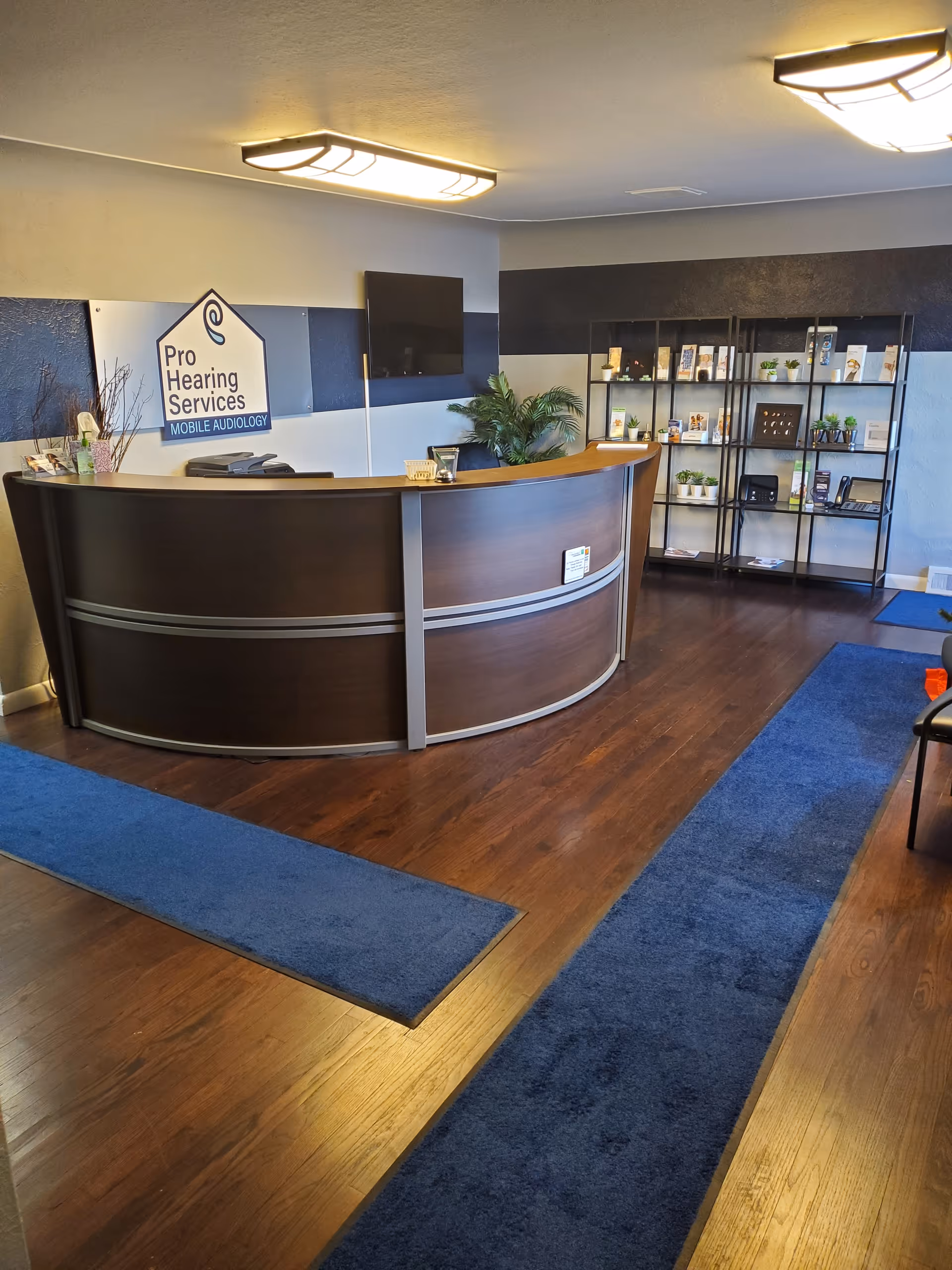 Reception area featuring curved dark wood desk, brochure shelves, and blue carpet runners.