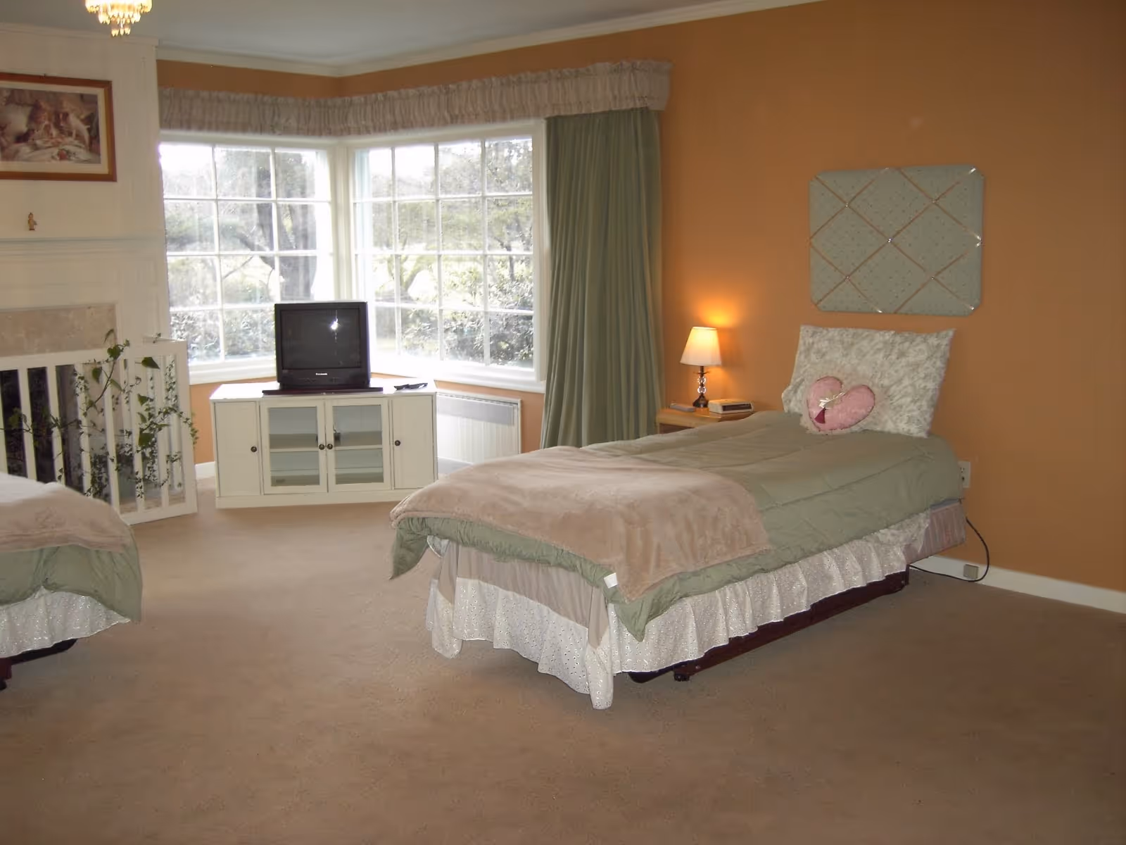Two twin beds in a warmly lit senior living bedroom with a window.