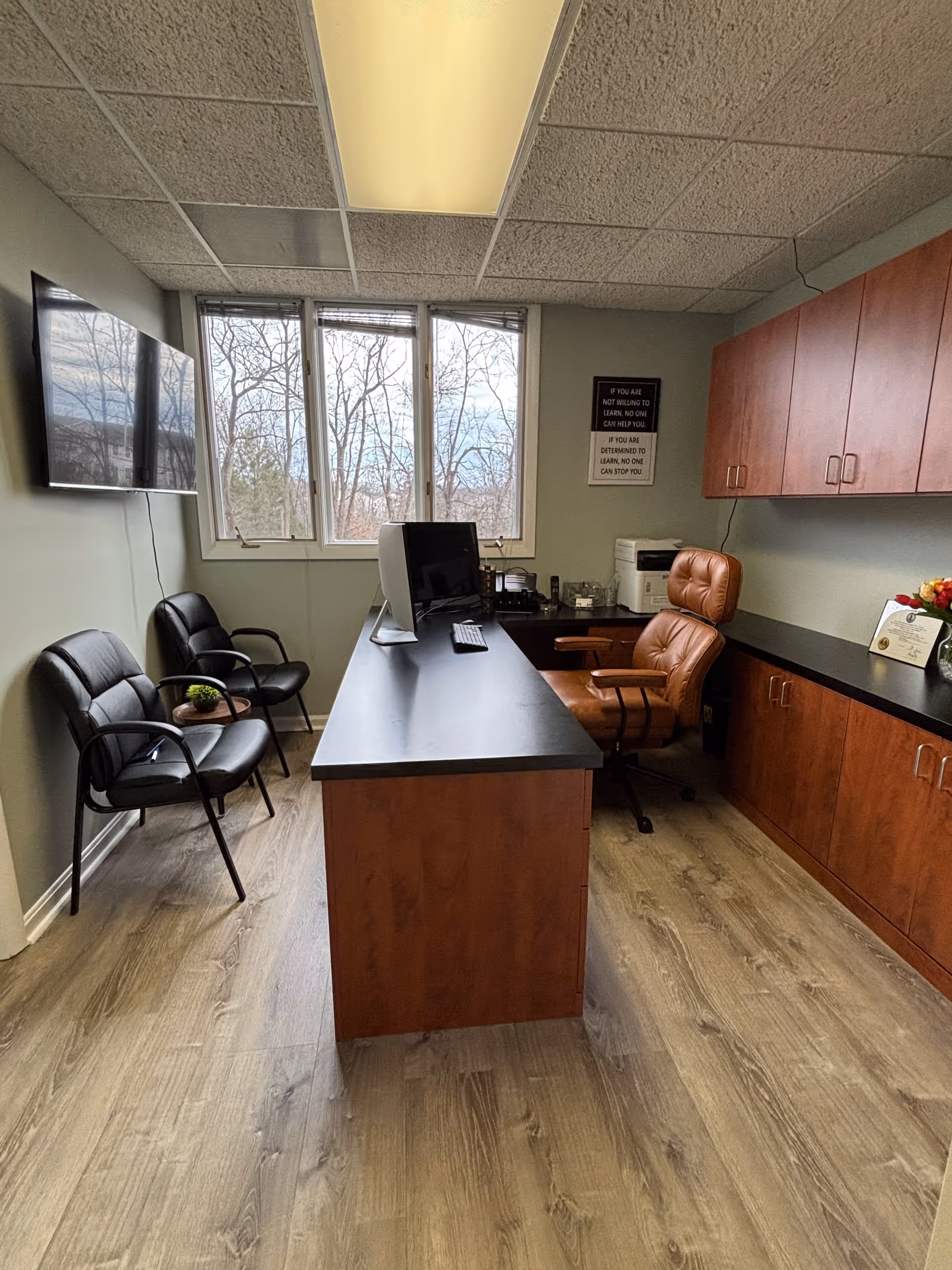 Reception desk with computer and leather chair in an office with cabinets.