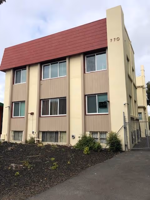 Three-story beige building with a red roof and the number 770 beside a gated walkway.