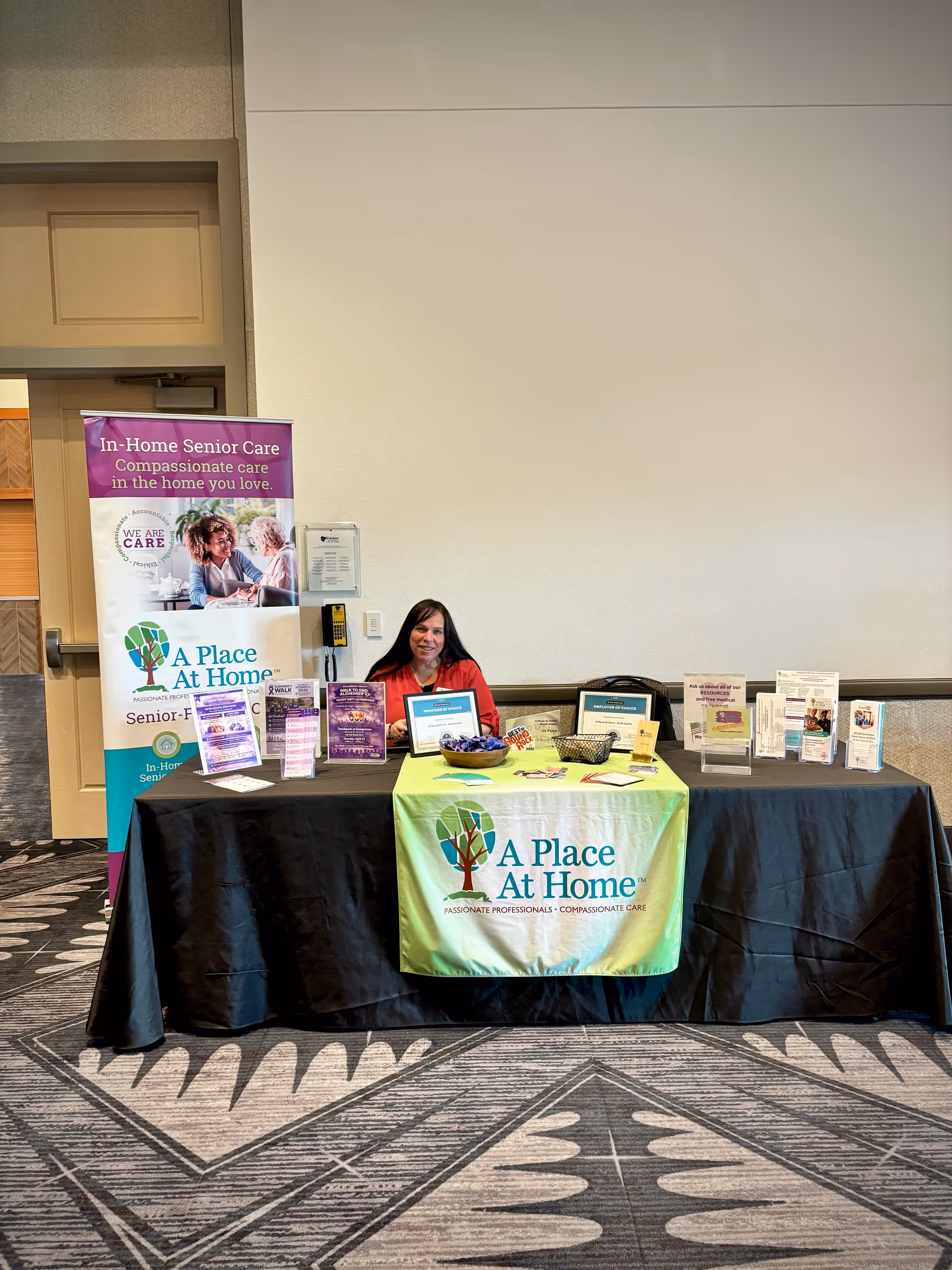 A person sits at a promotional table with banners and brochures for A Place At Home.