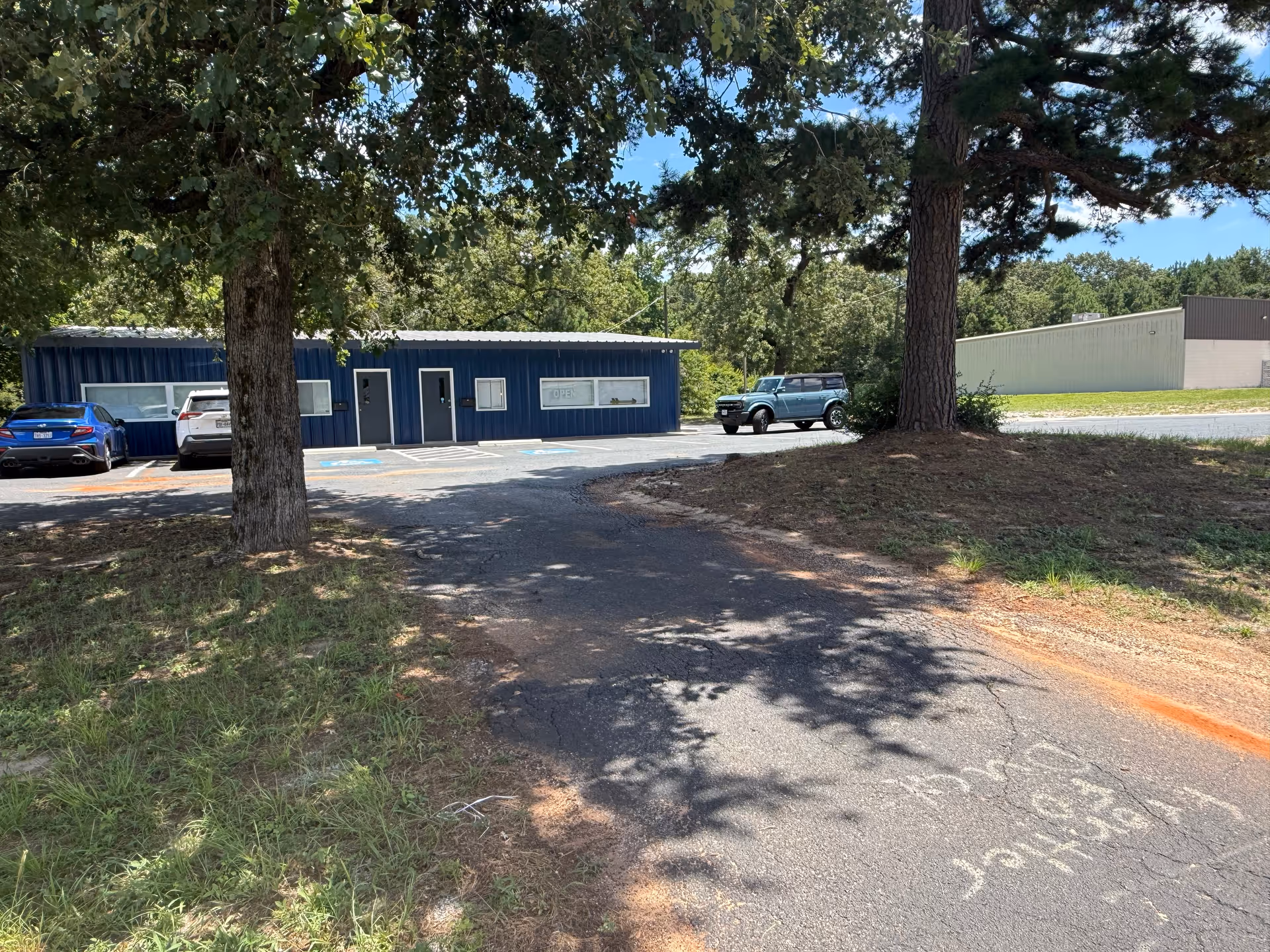 Blue single-story building with parked cars in a parking lot shaded by trees.