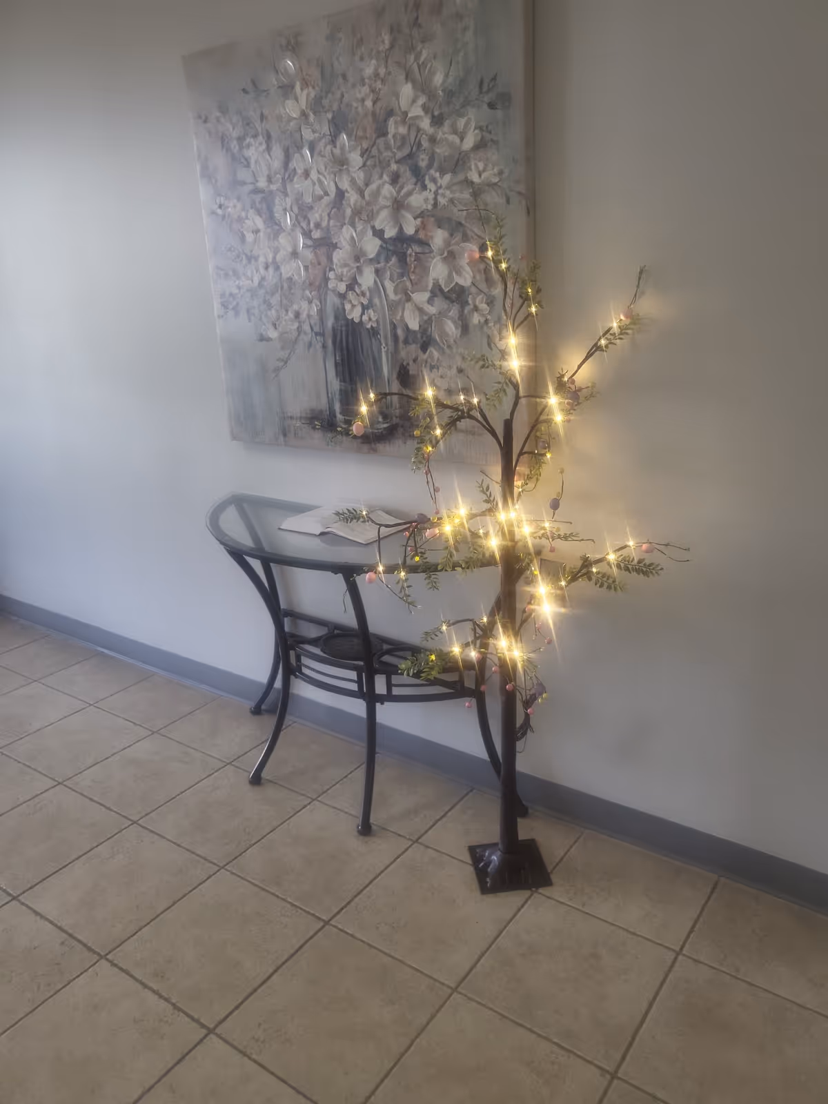 A lit decorative tree stands beside a curved console table in a hallway.