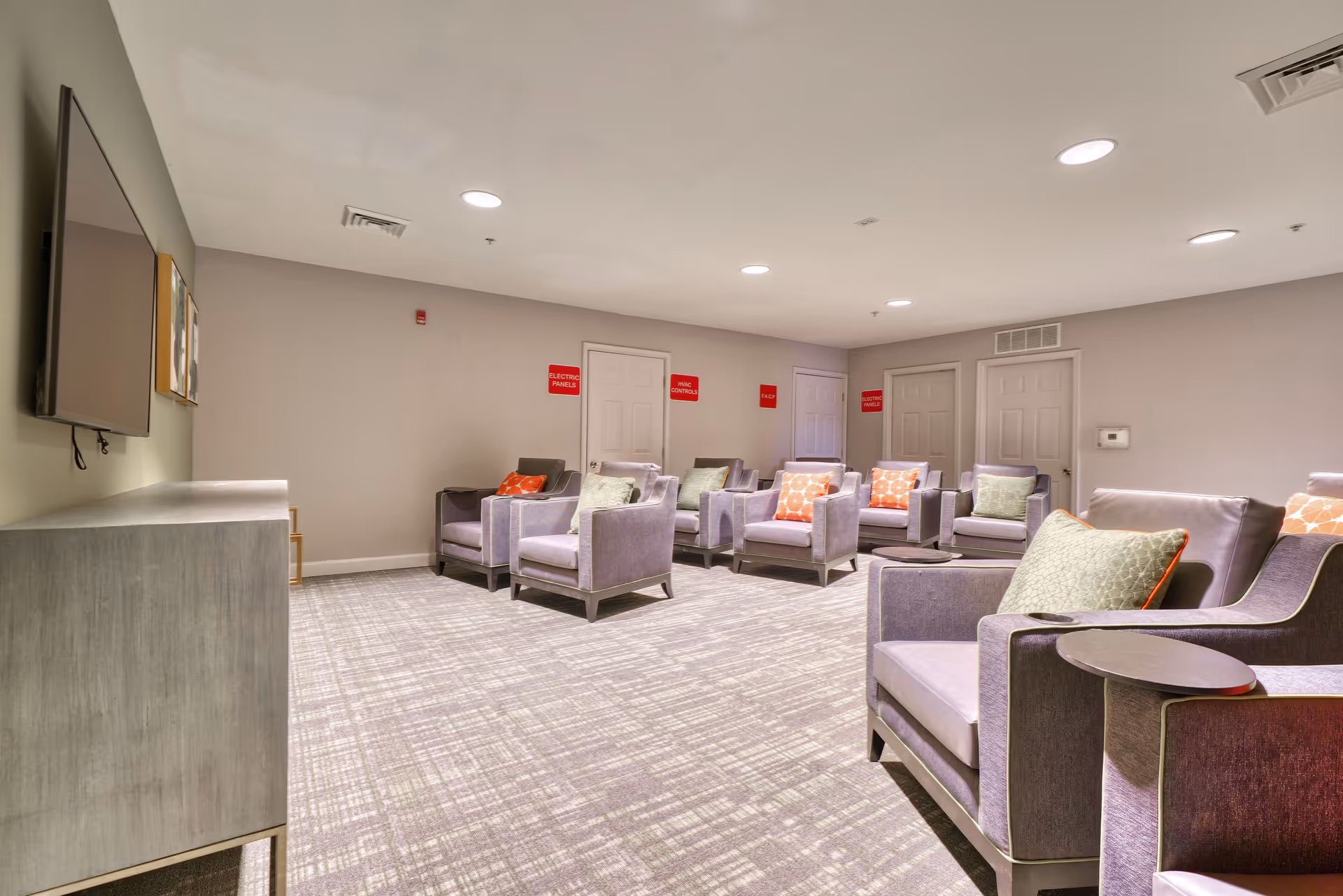 Willow Manor at Fair Hill Farm lounge with gray chairs, tables, and a wall-mounted TV.