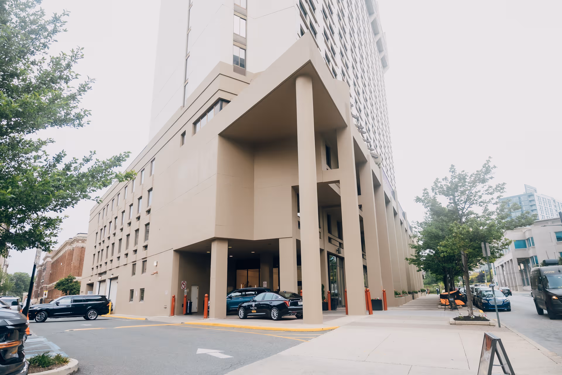 Tall beige building exterior with a covered entrance and parked cars along the street.