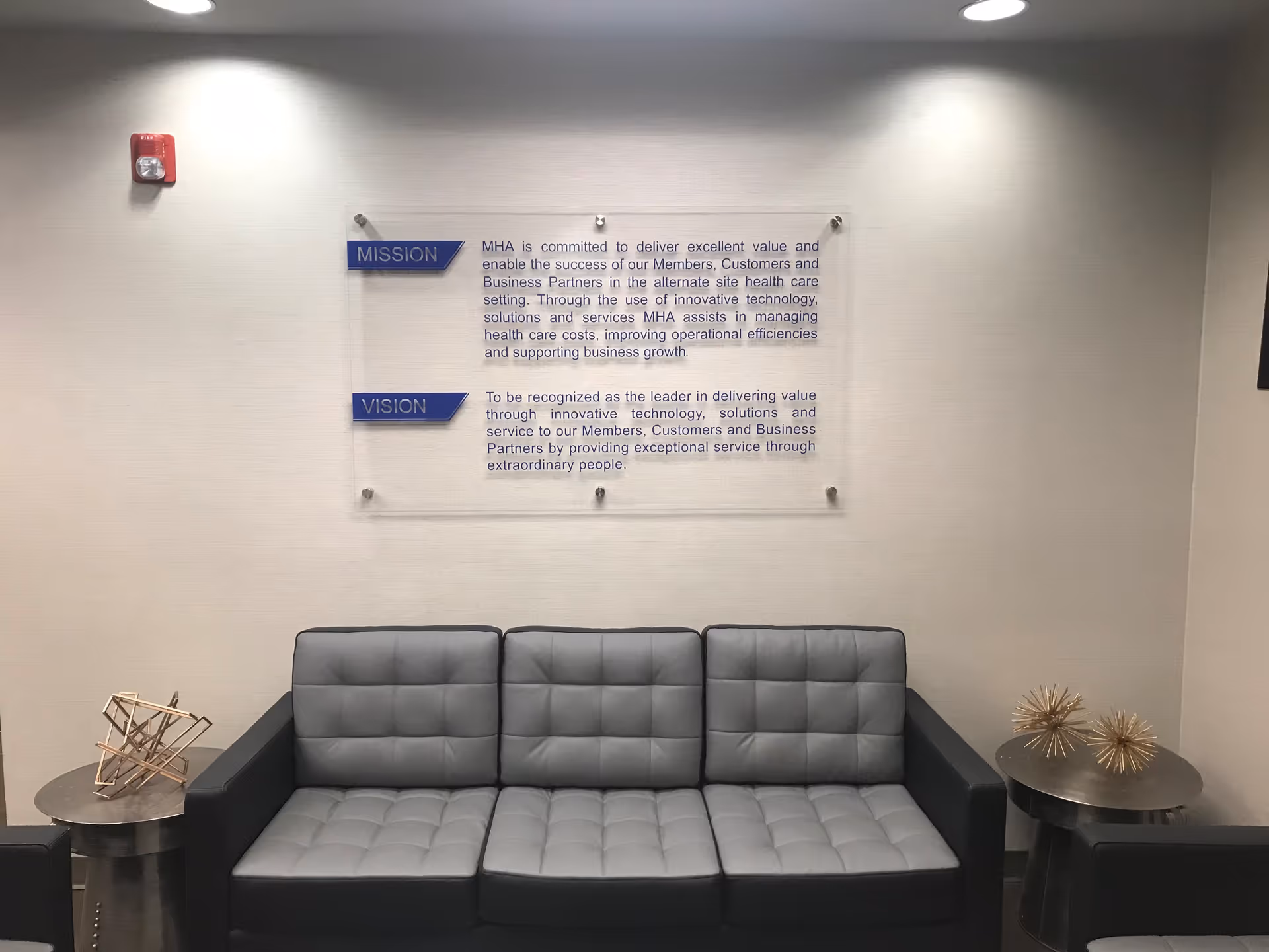 Waiting area with gray tufted sofa, side tables, and wall mission/vision plaque