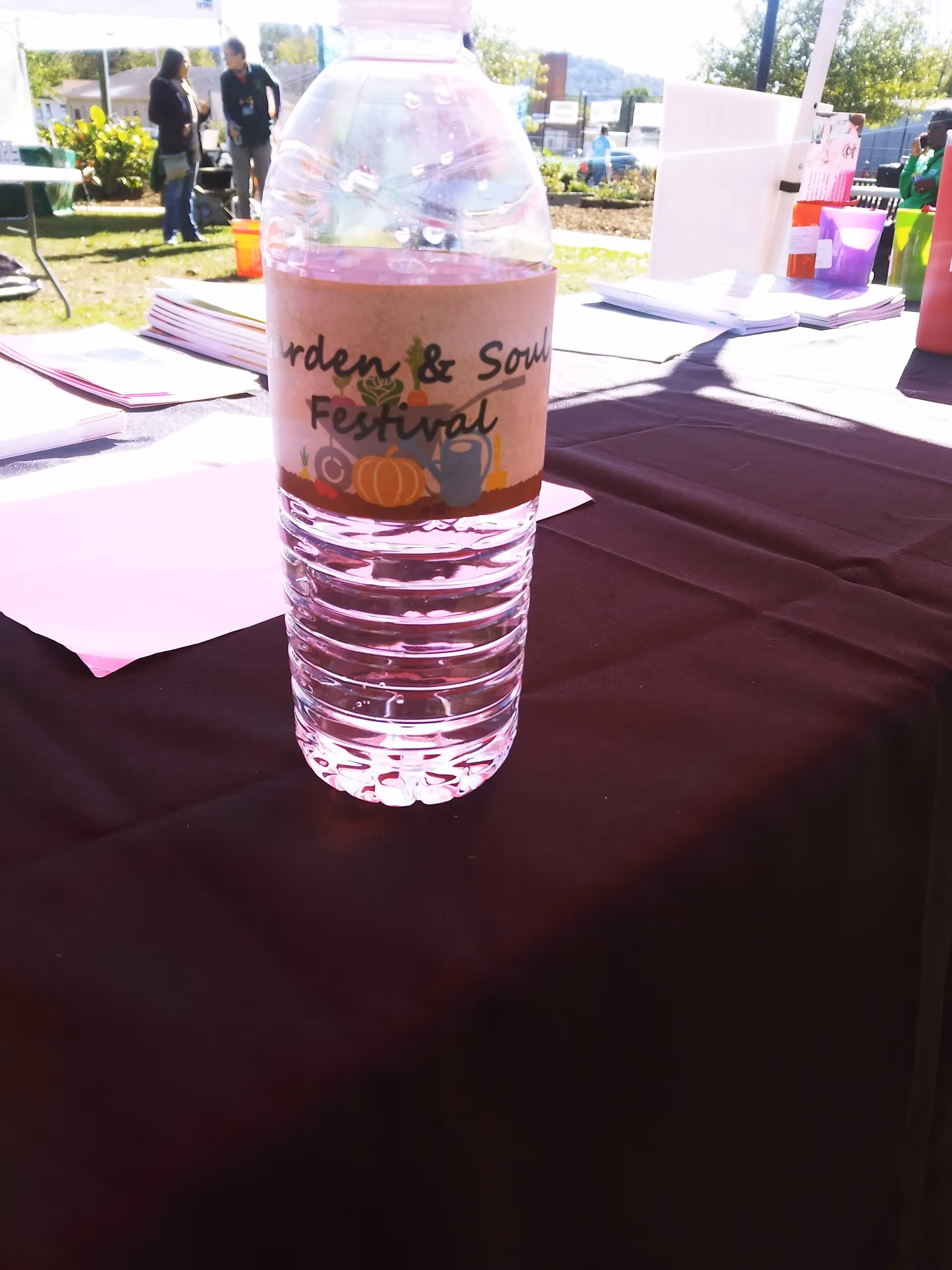 Plastic water bottle with festival label sits on a table outdoors at a community event.