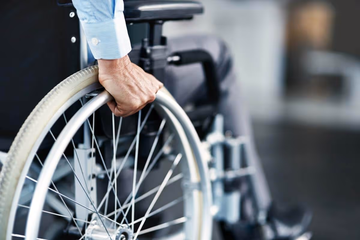 Close-up of a hand gripping the wheel of a wheelchair inside a facility.