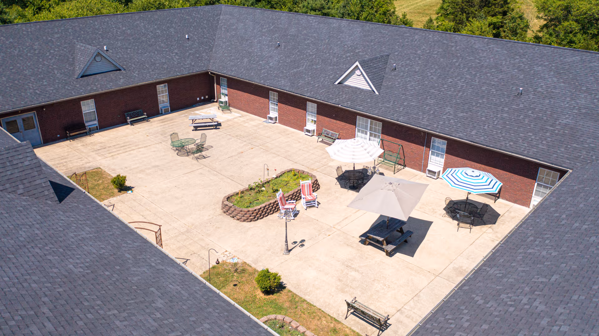 Aerial view of a courtyard in a brick senior living building with tables, umbrellas, and benches.